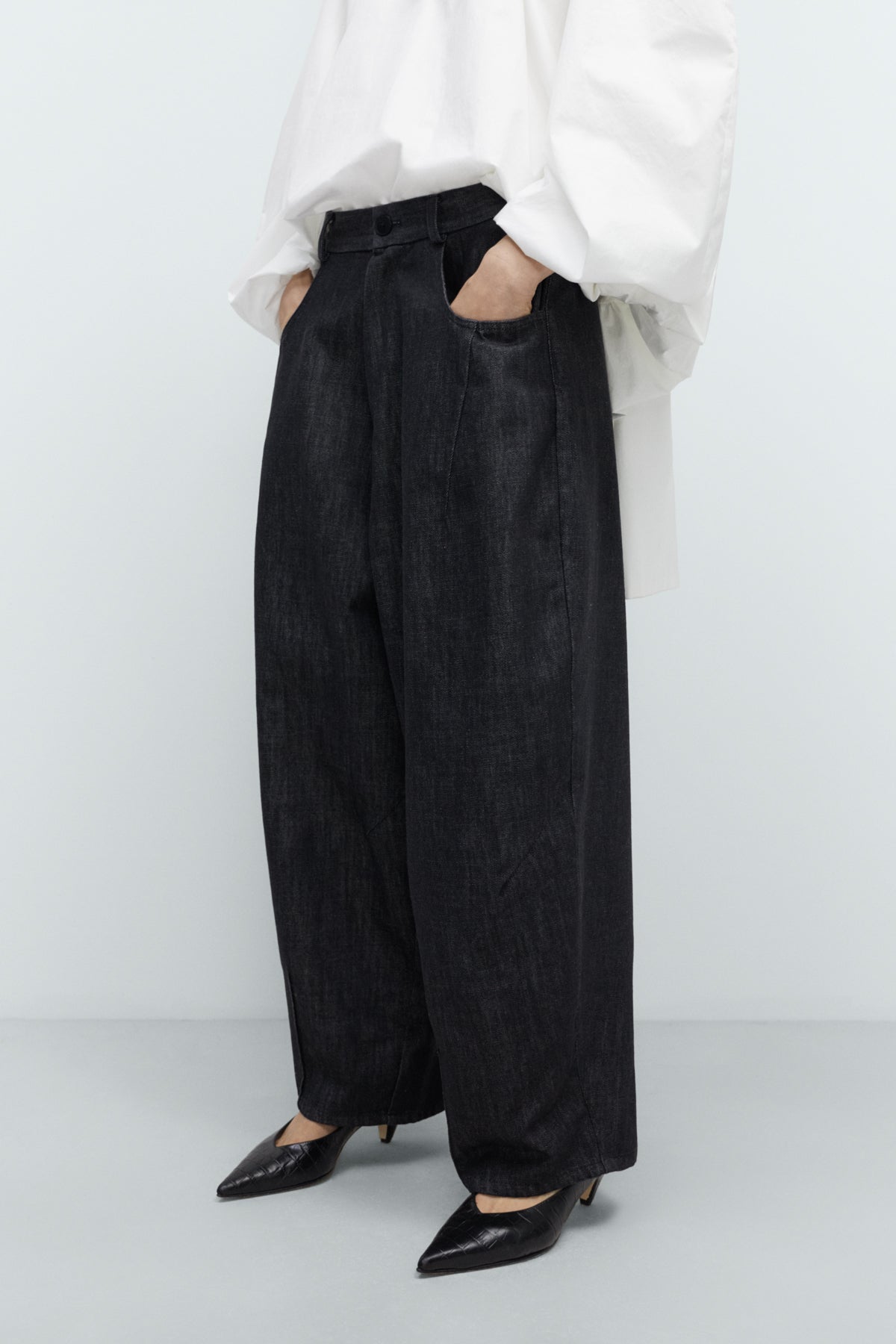 Person wearing black wide-leg pants and a white top on a white background