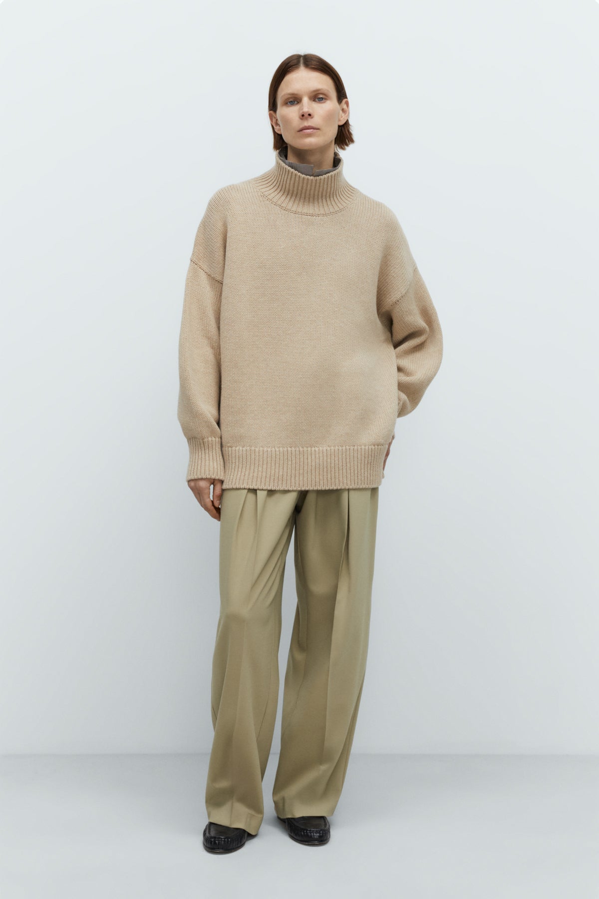 Person wearing a beige sweater and pants against a white background