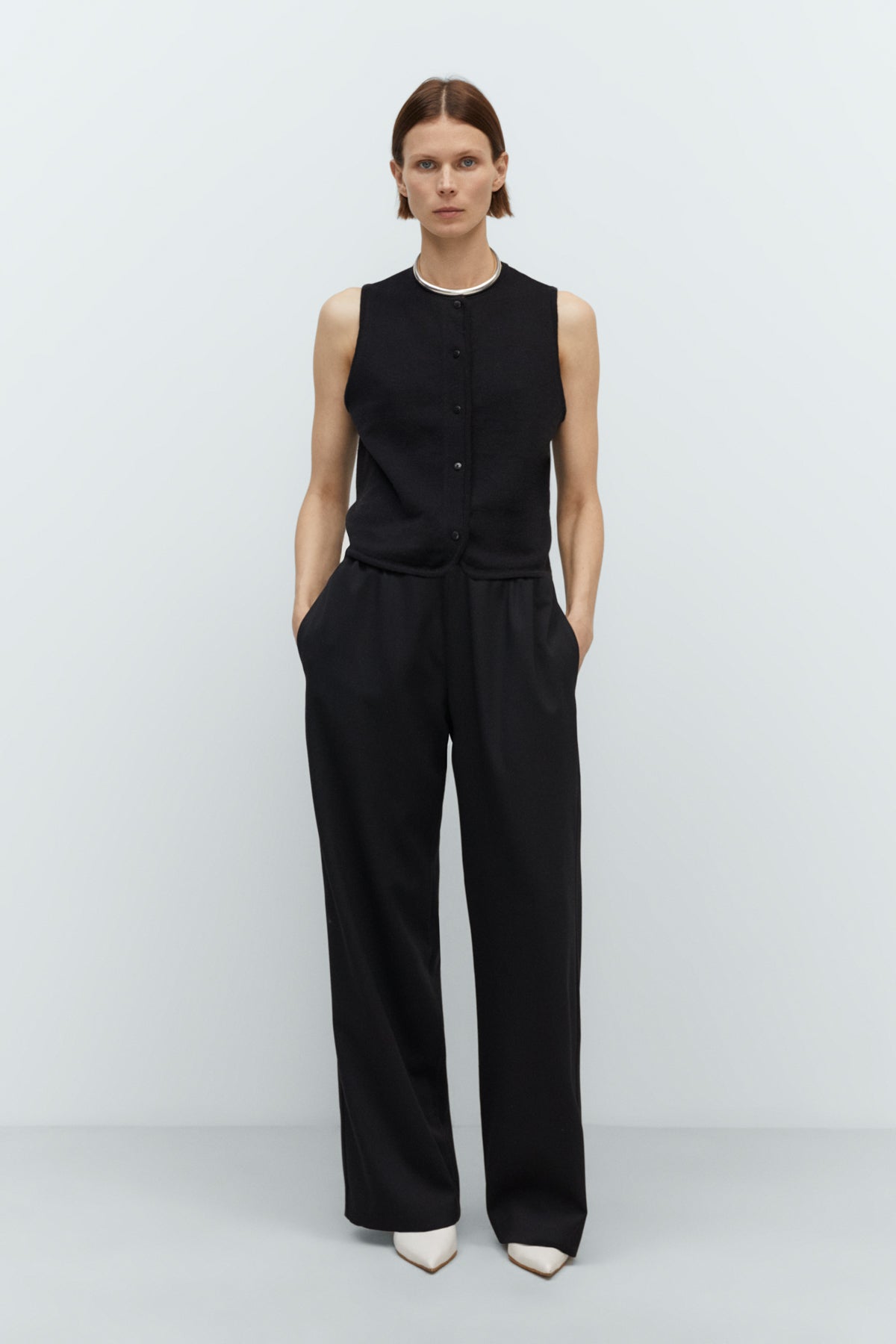 Person wearing a black sleeveless top and black pants on a white background