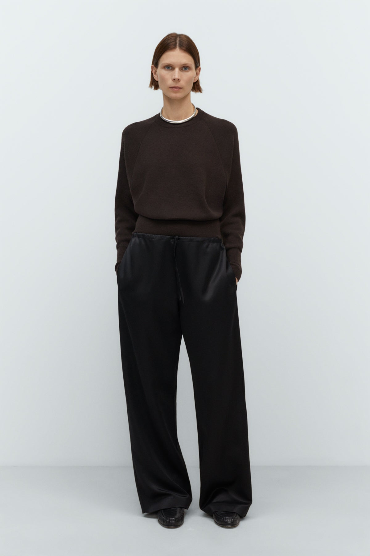 Person wearing black wide-leg pants and a brown top on a white background