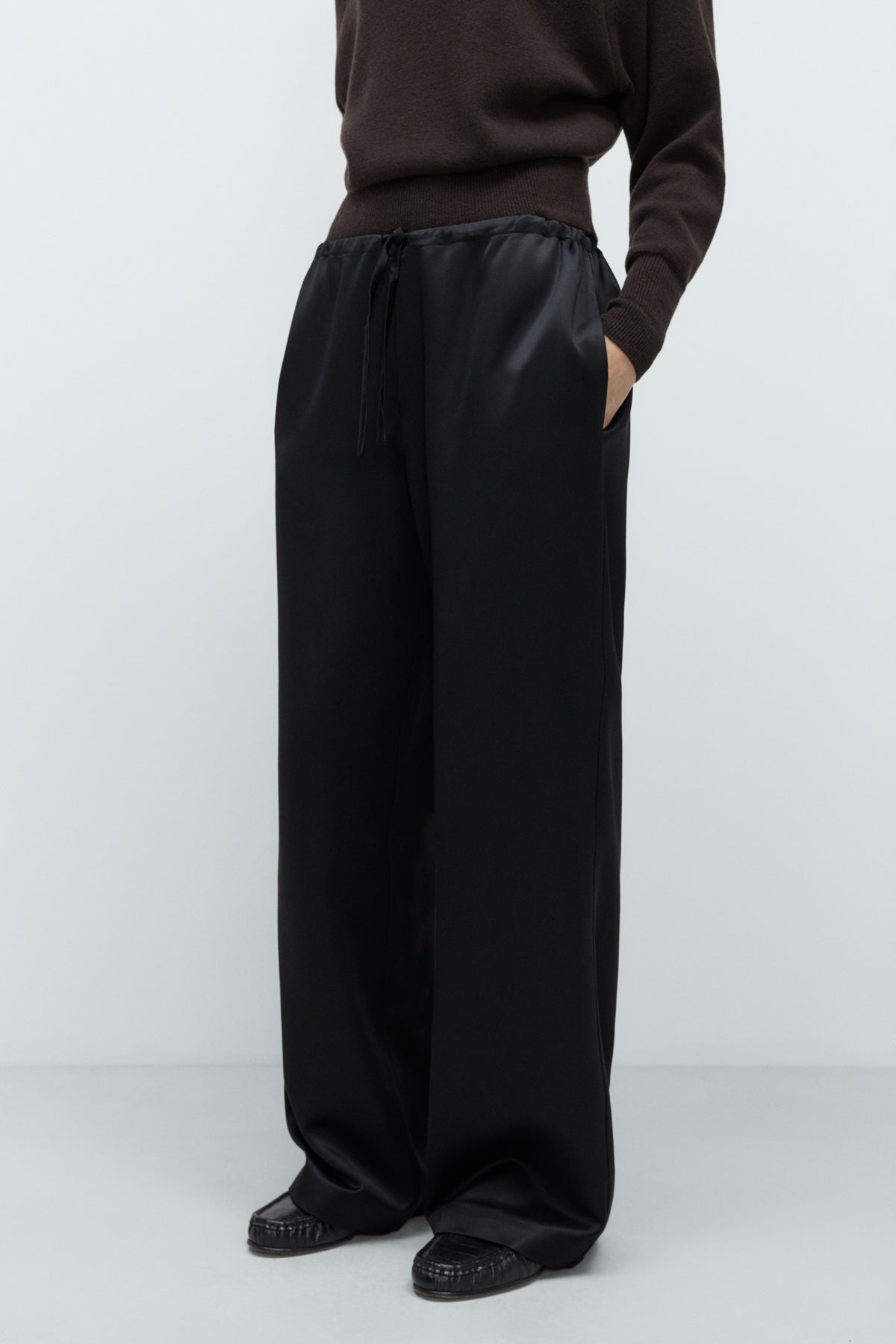 Person wearing black wide-leg pants and a brown top on a white background