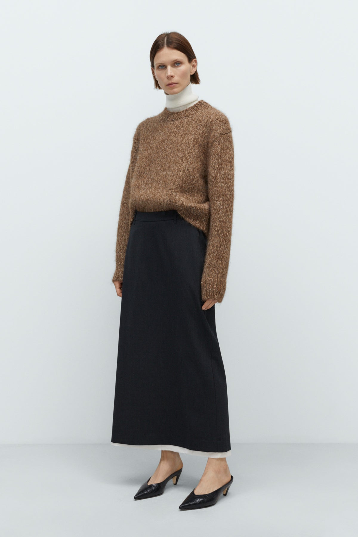 Woman wearing a brown sweater and black skirt on a white background