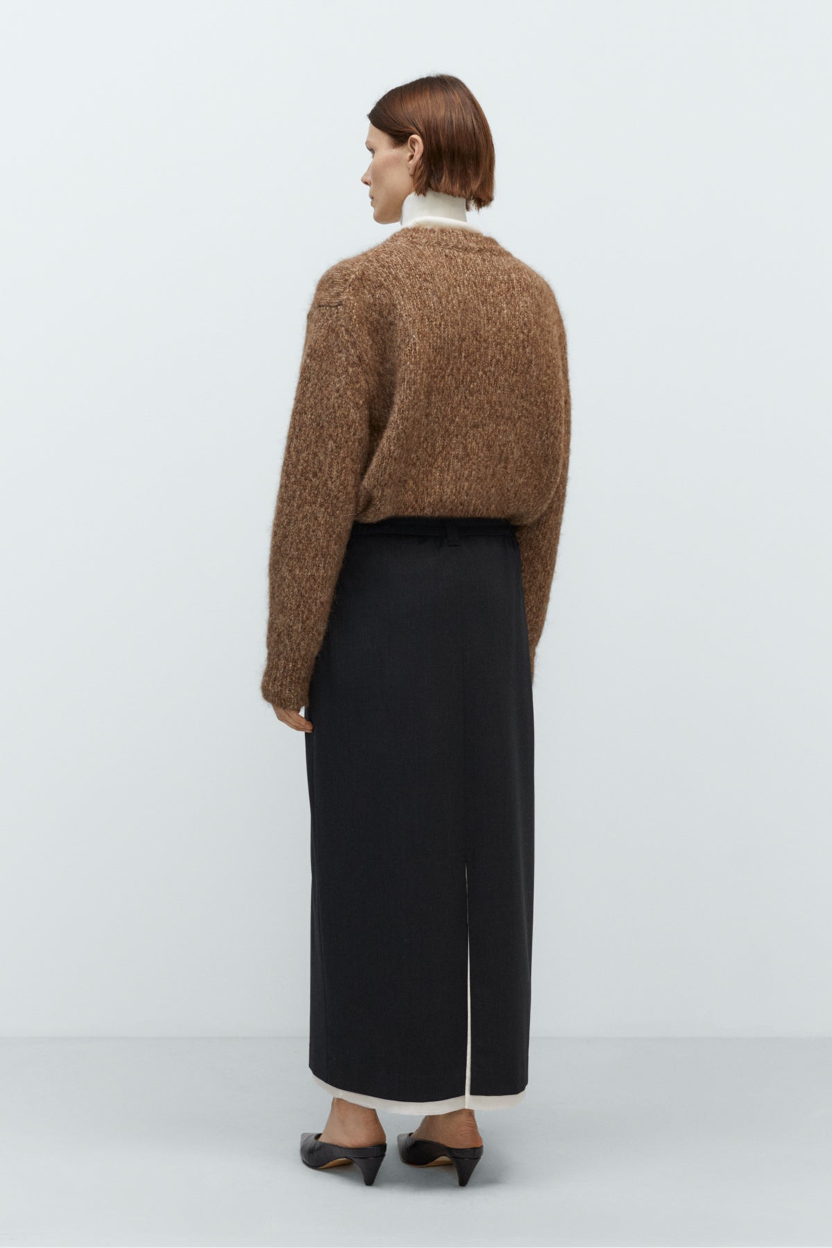 Person wearing a brown sweater and black pants on a white background