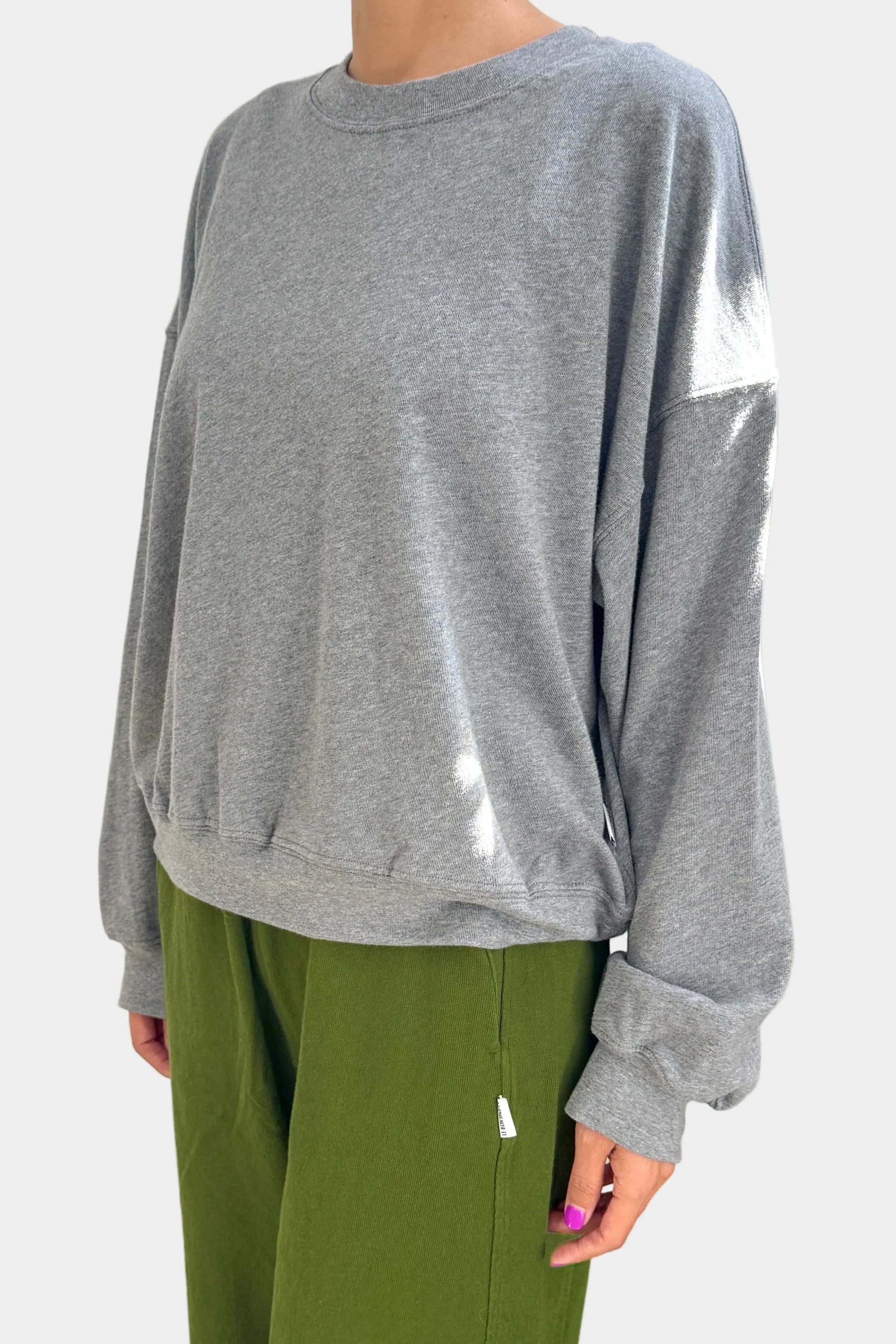 Person wearing a gray sweatshirt and green pants on a plain background