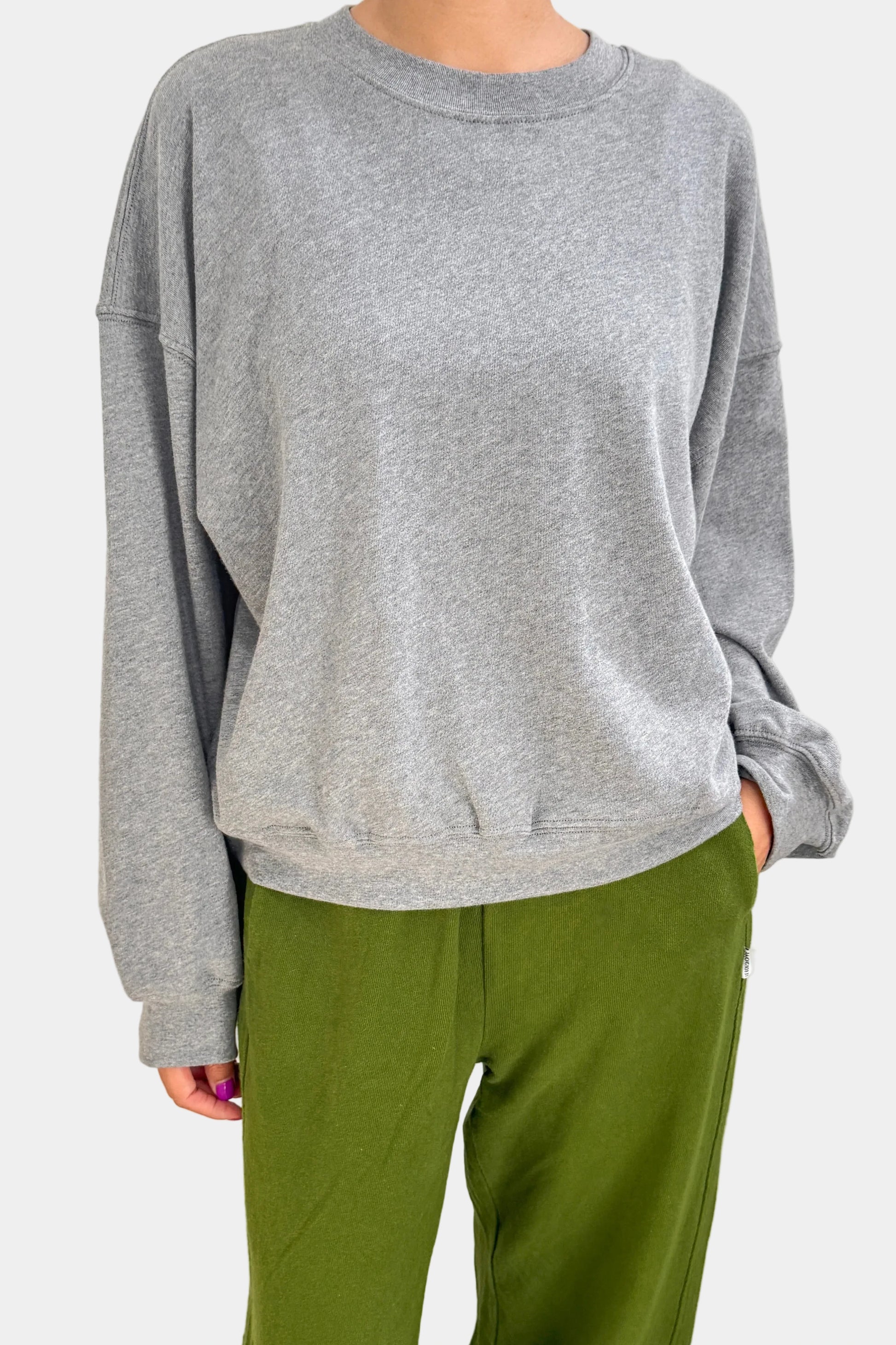 Person wearing a gray sweatshirt and green pants on a plain background