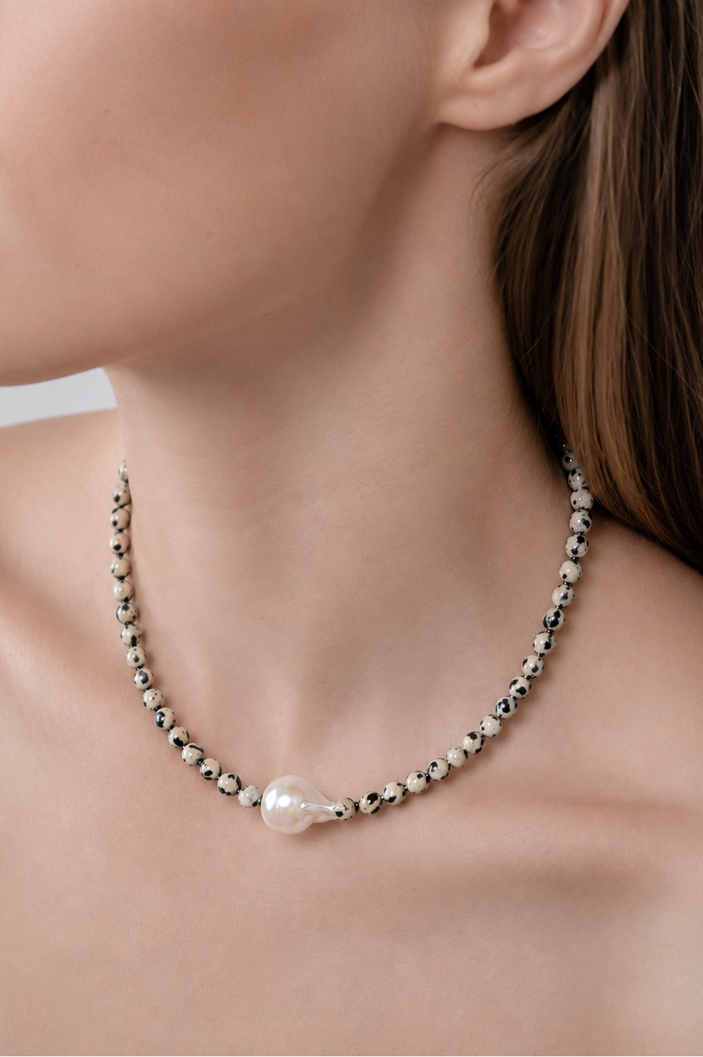 Close-up of a necklace with jasper stones and a single Baroque  pearl on a person's neck