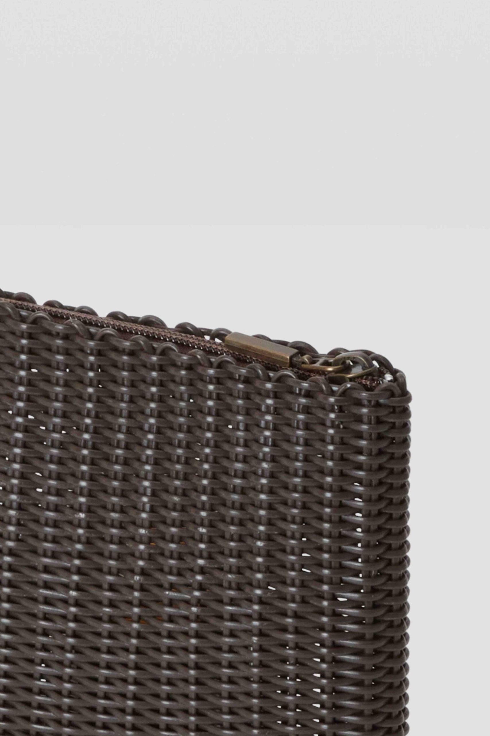 Close-up of a woven clutch bag with a gold clasp on a light gray background