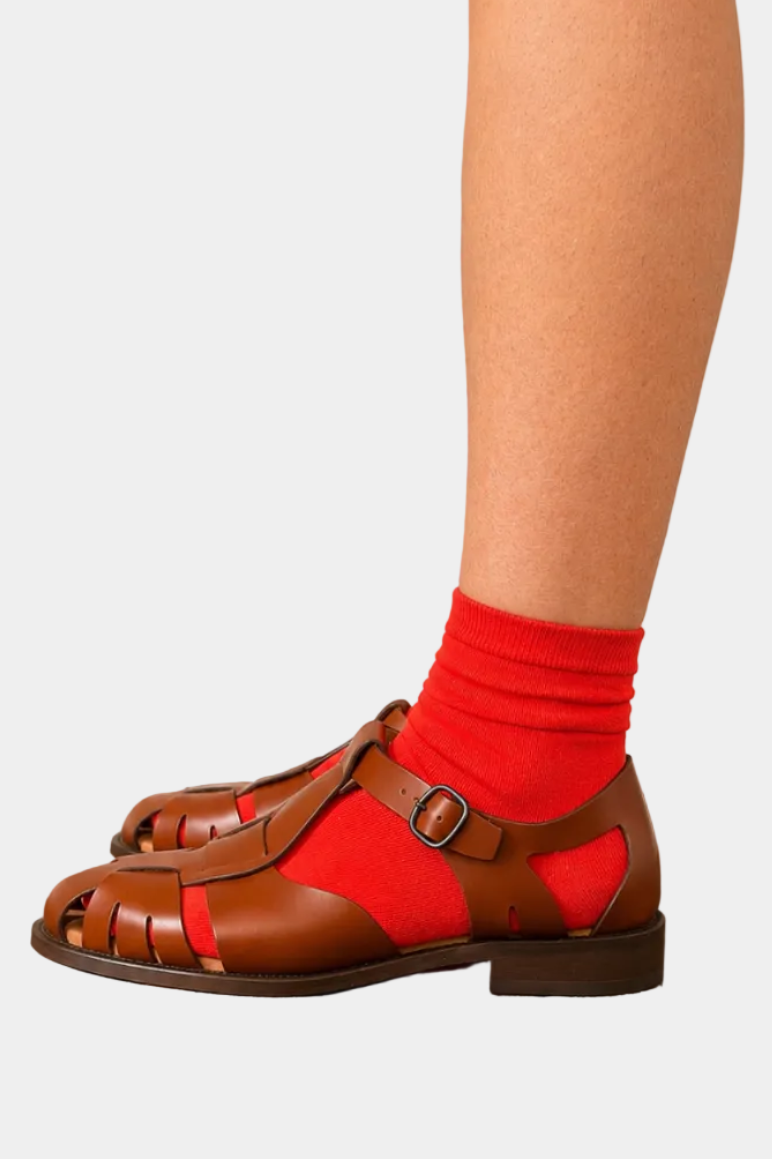 Brown sandals worn with red socks against a plain background