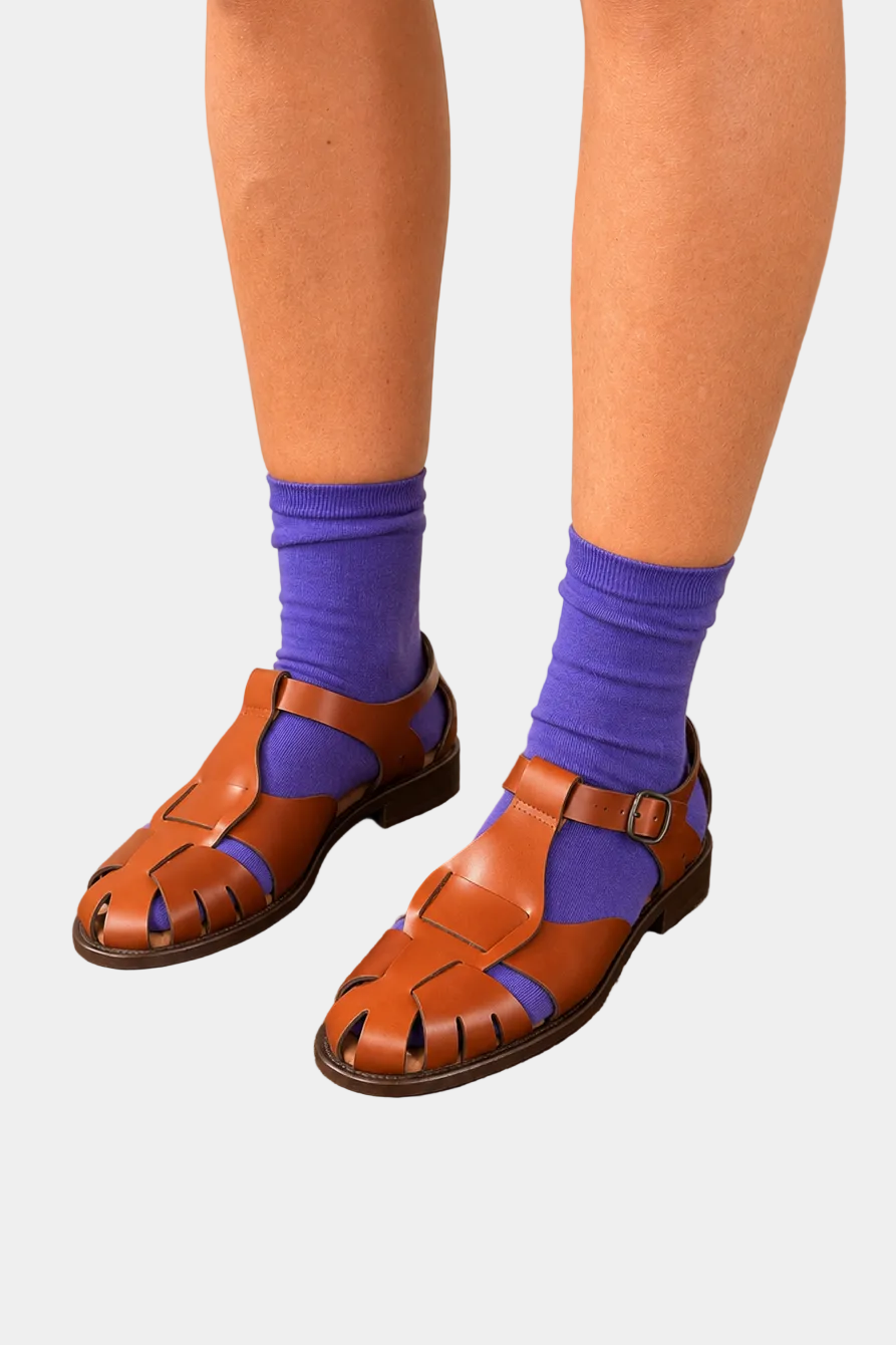 Brown sandals worn with purple socks against a plain background