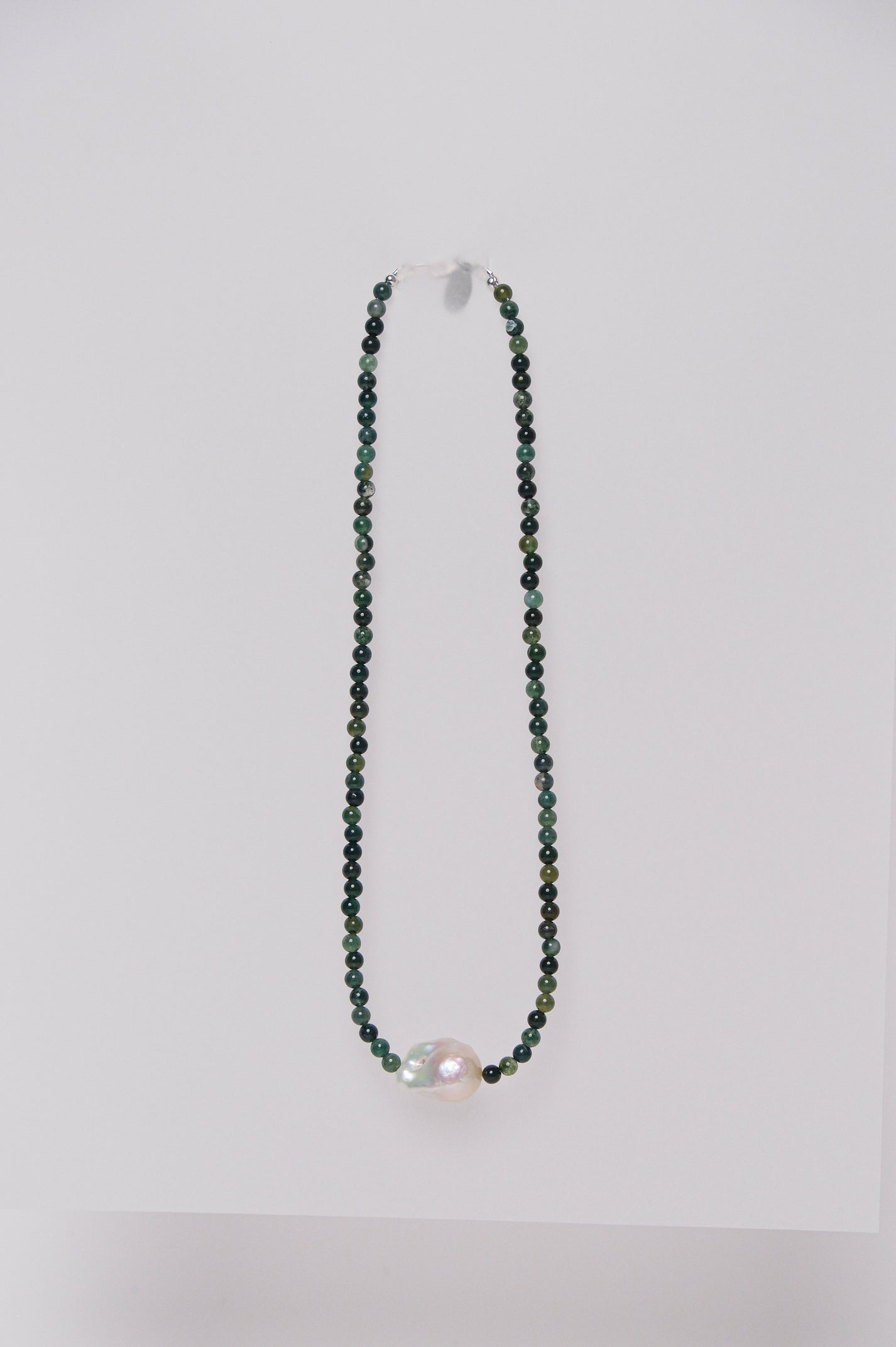 A beaded necklace with green agate stones and a single baroque fresh water pearl, displayed against a white background.