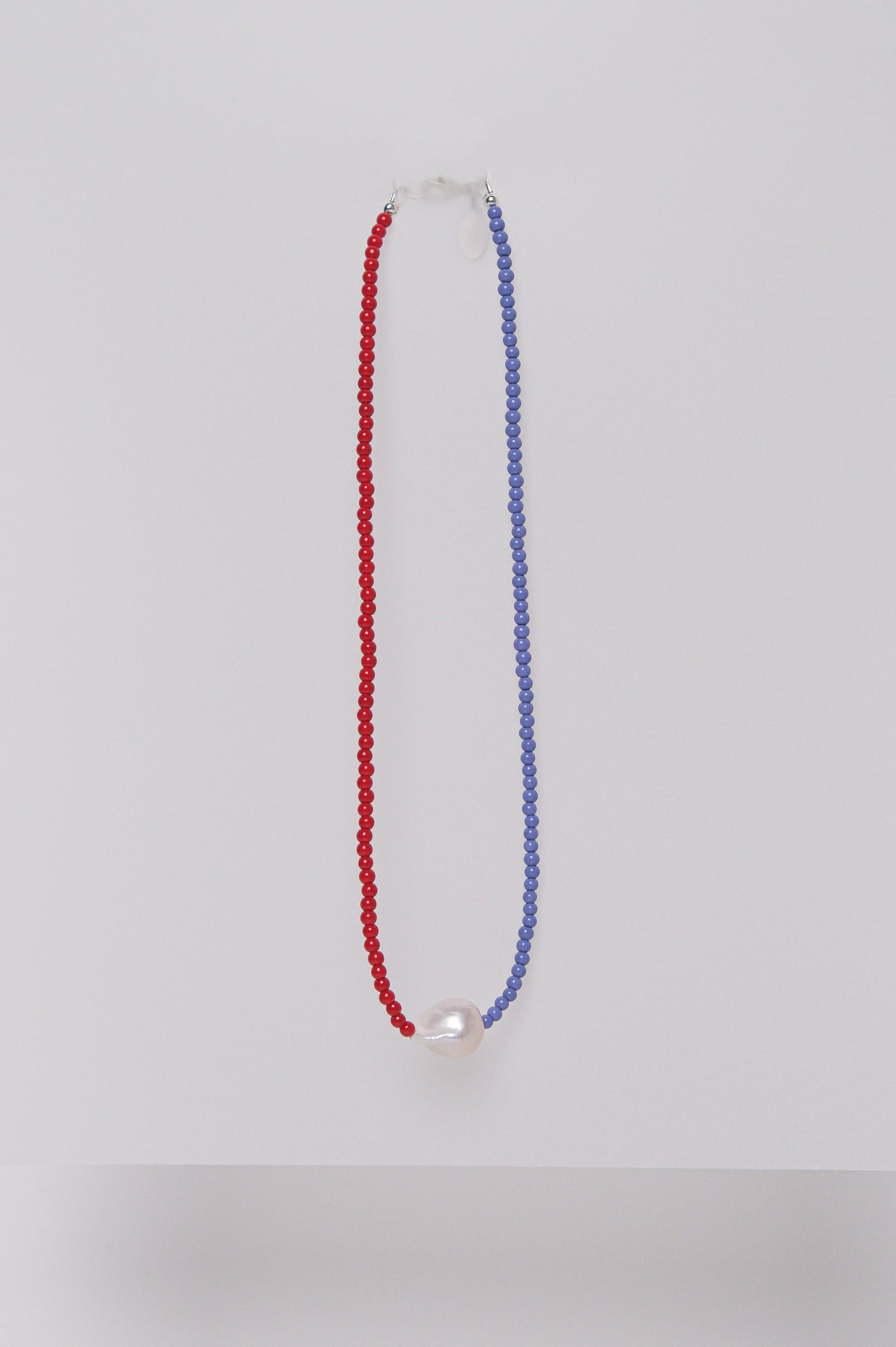 A two-tone beaded necklace with red and purple beads and a single pearl, displayed against a white background.