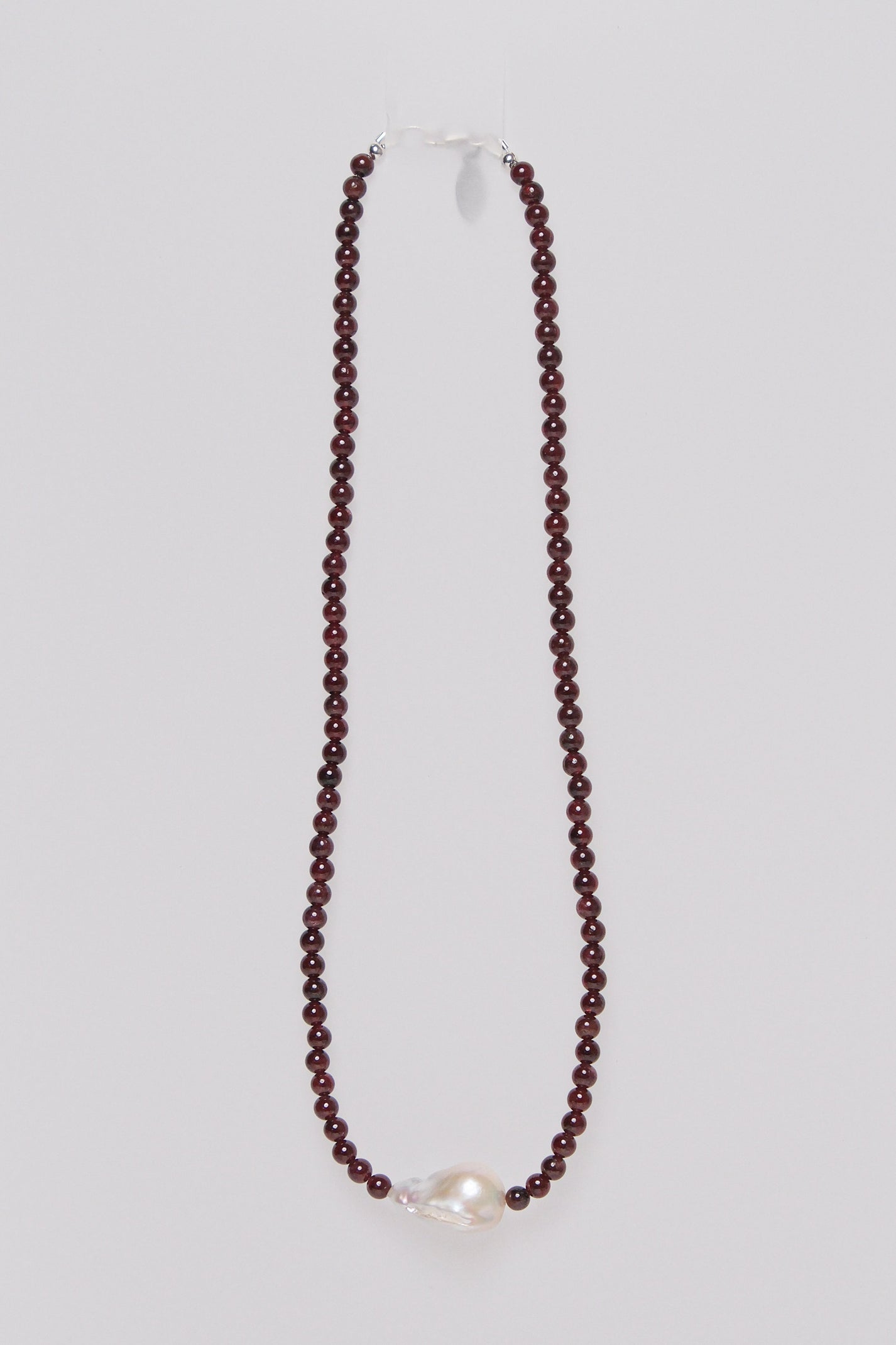 A necklace with red garnet beads and a single baroque fresh water pearl.
