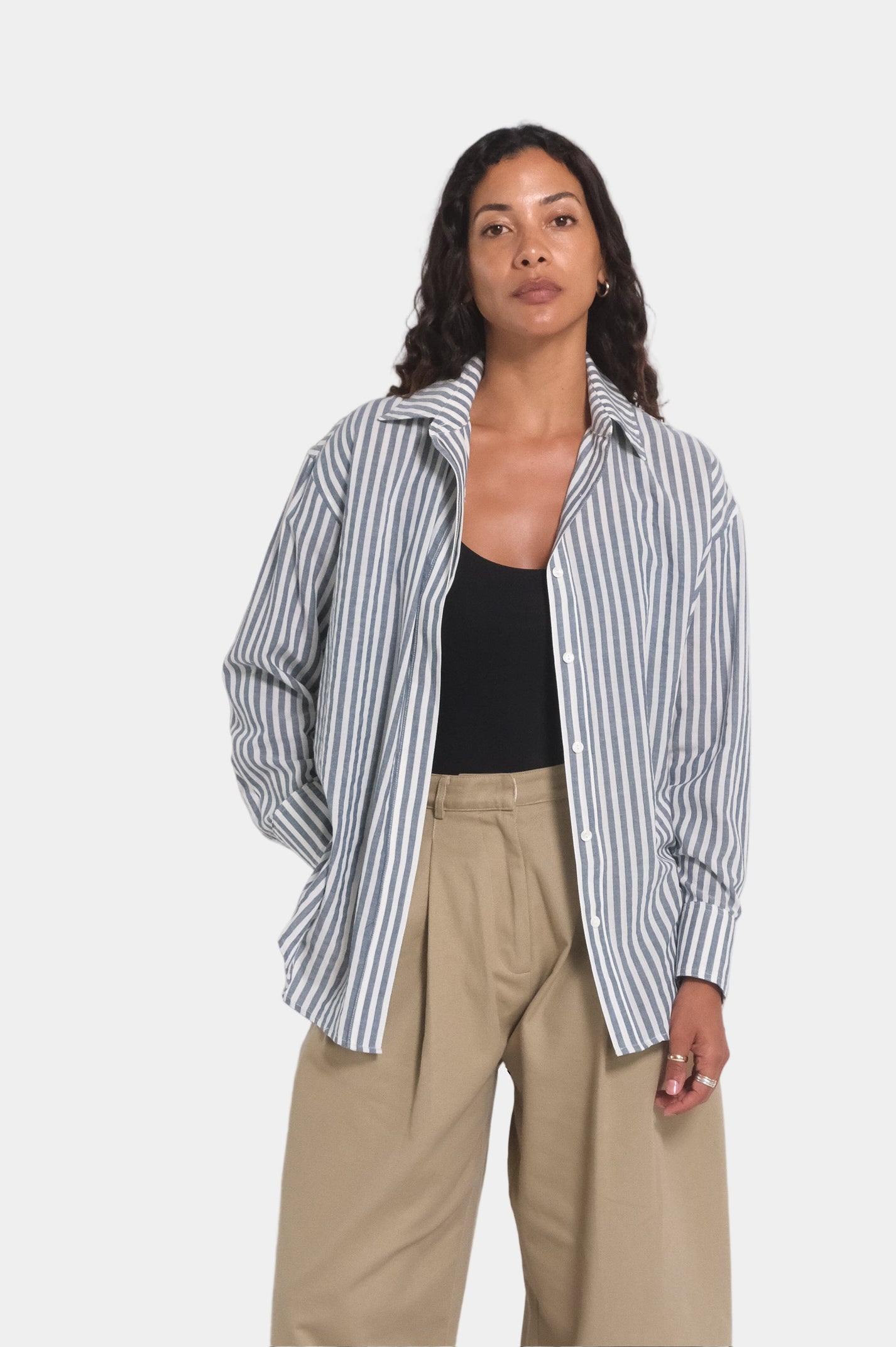 a women wearing a grey blue and white stripe shirt and beige trousers with a black singlet