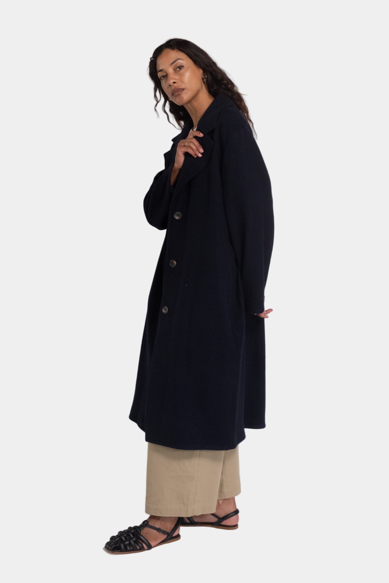 A woman modeling a navy longline tailored wool overcoat with notched lapels and a mid-calf length.