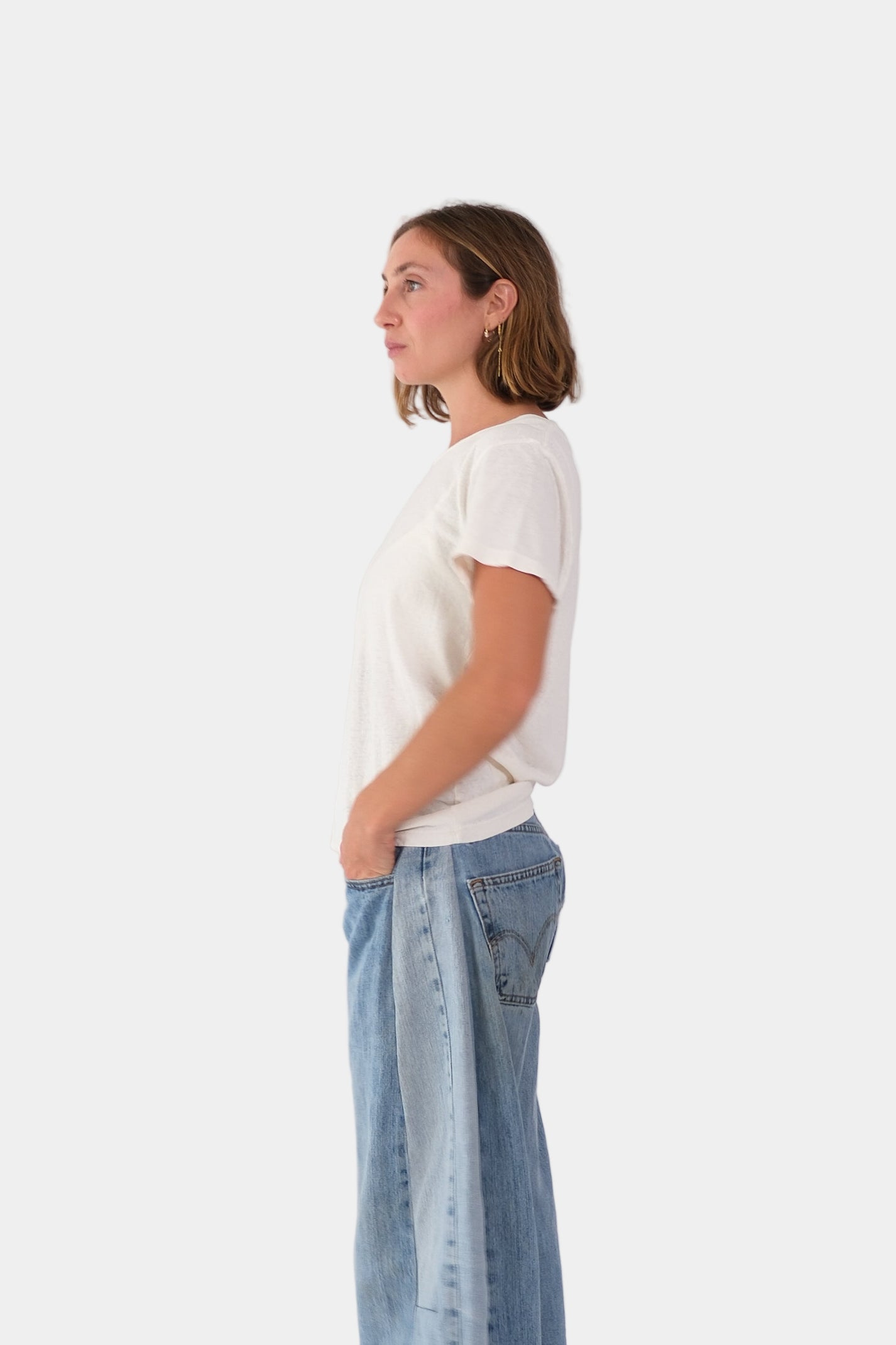 a person wearing the LOREL TEE in white with blue denim jeans on a plain background