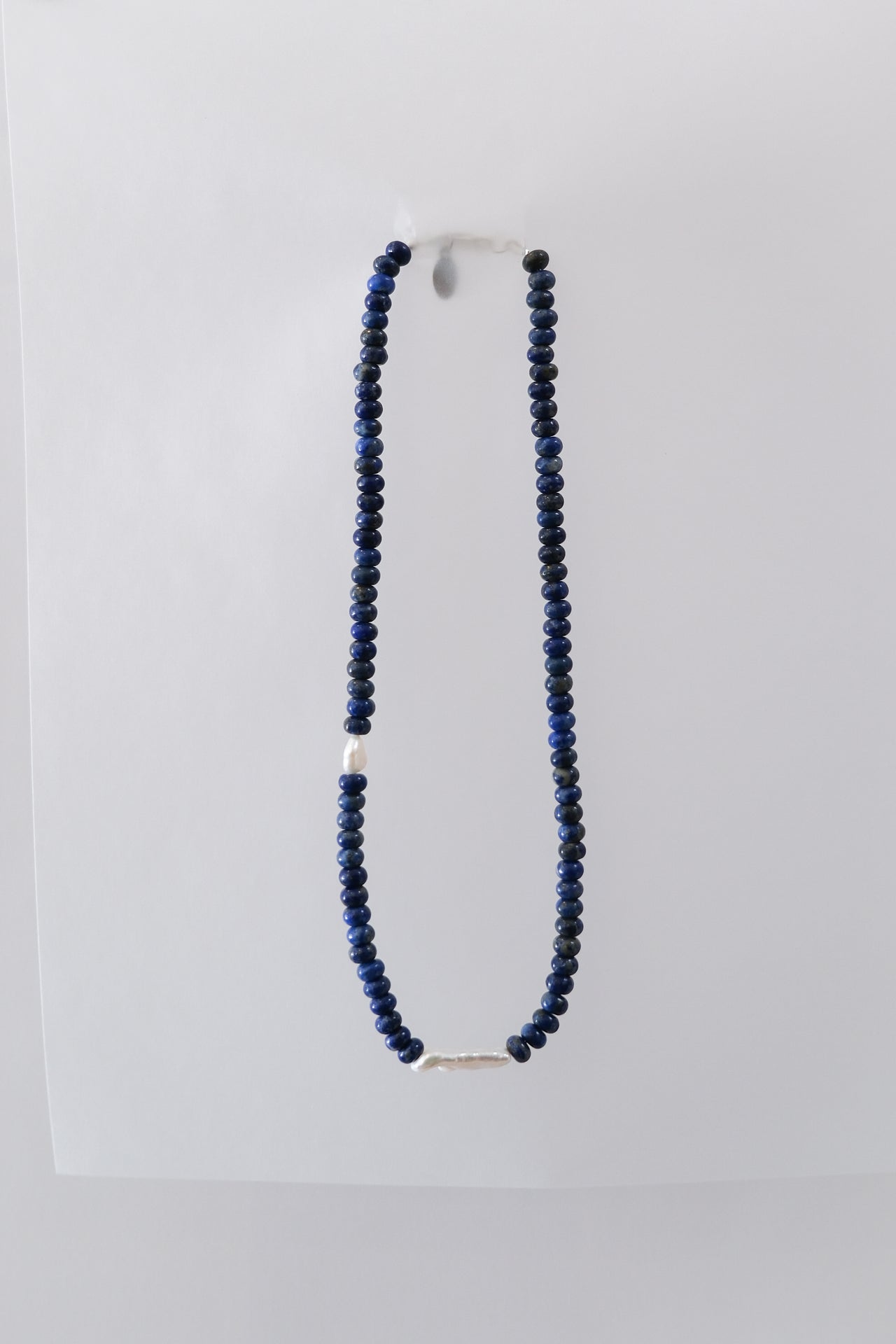 A lapis lazuli beaded necklace with a silver clasp and fresh water pearls, displayed against a white background.