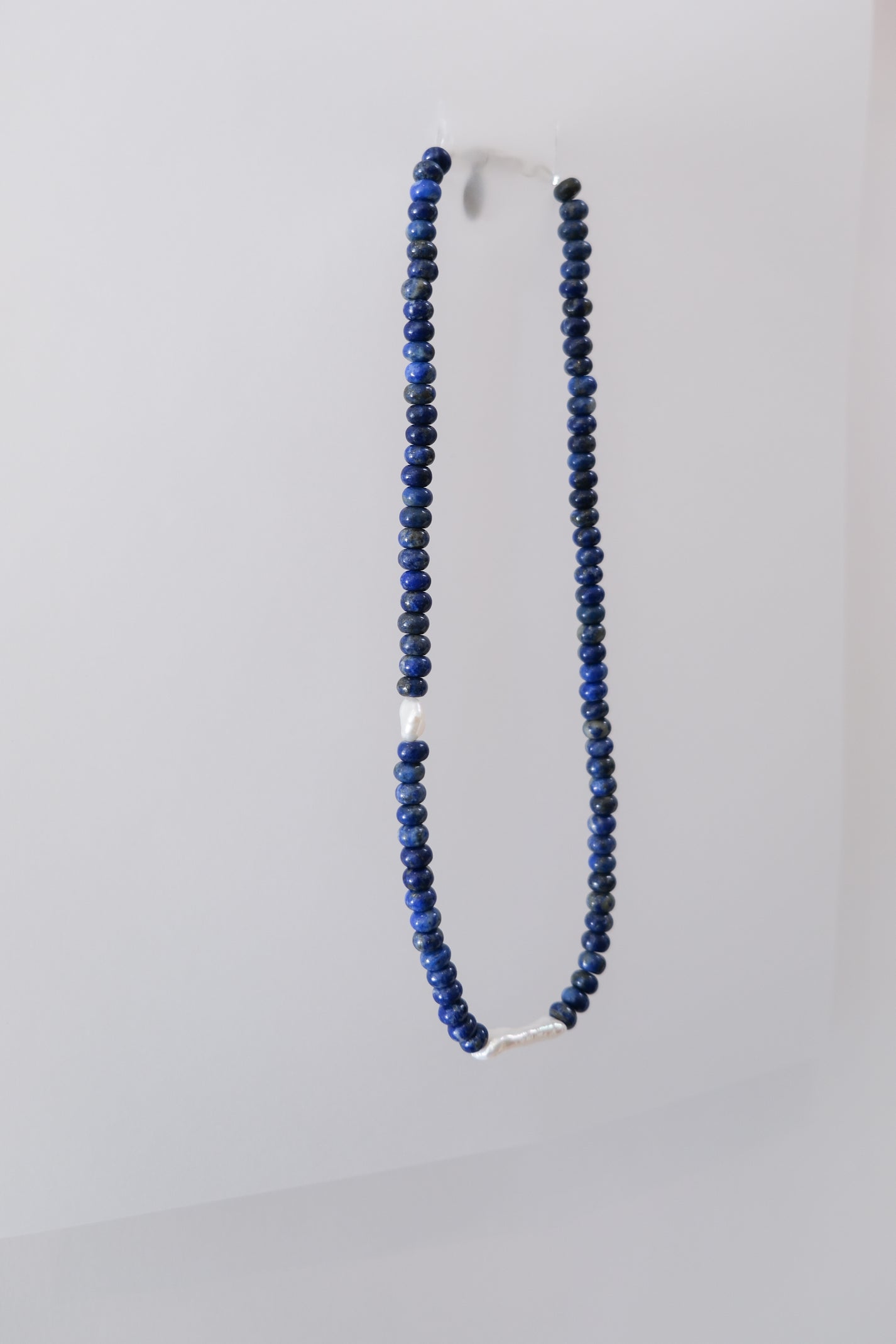 A lapis lazuli beaded necklace with a silver clasp and fresh water pearls, displayed against a white background.