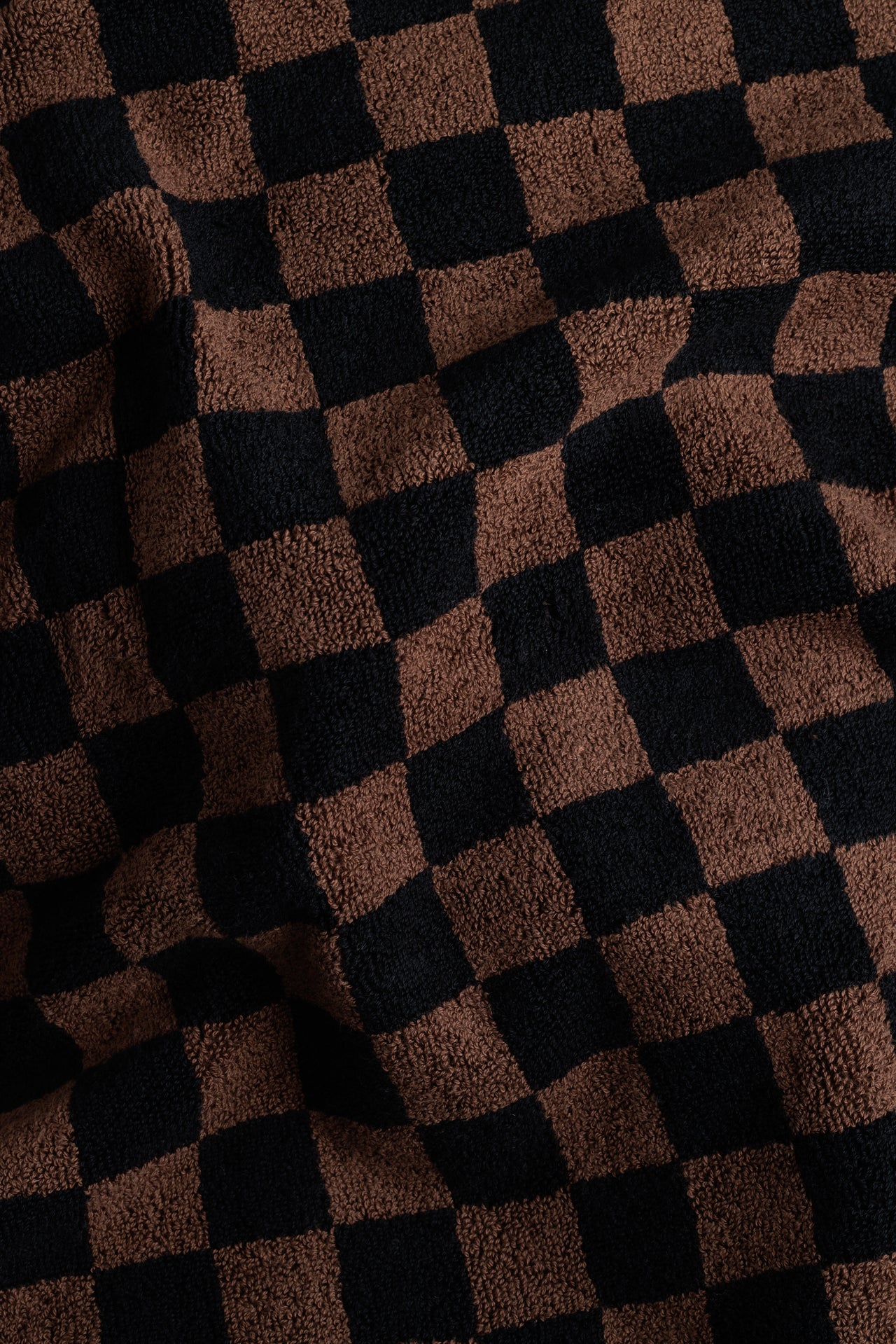 Folded brown and black checkered pool towel on a light gray background