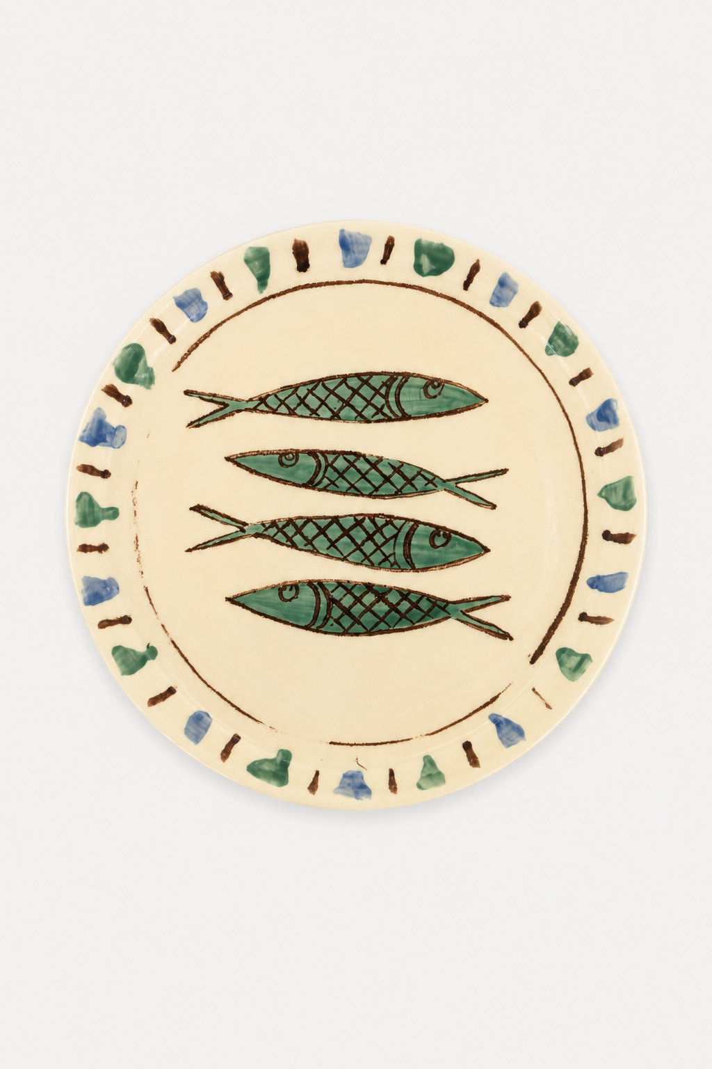 A Di Lunedi sardine plate with a cream-colored glaze, featuring three green sardines with black scales in the center and a decorative border of small blue and green hearts with brown dots.
