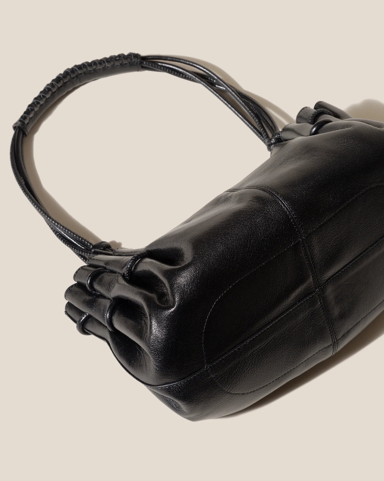 Black leather handbag with a textured handle on a beige background