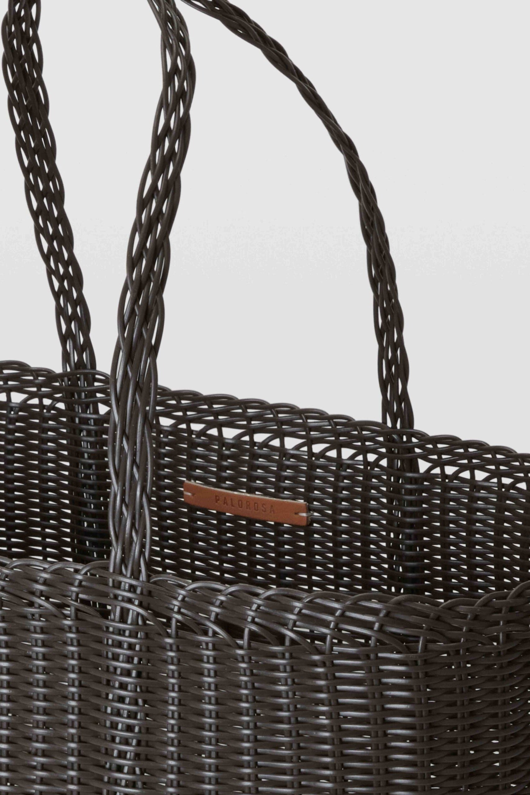 Close-up of a dark woven basket with a handle on a light gray background