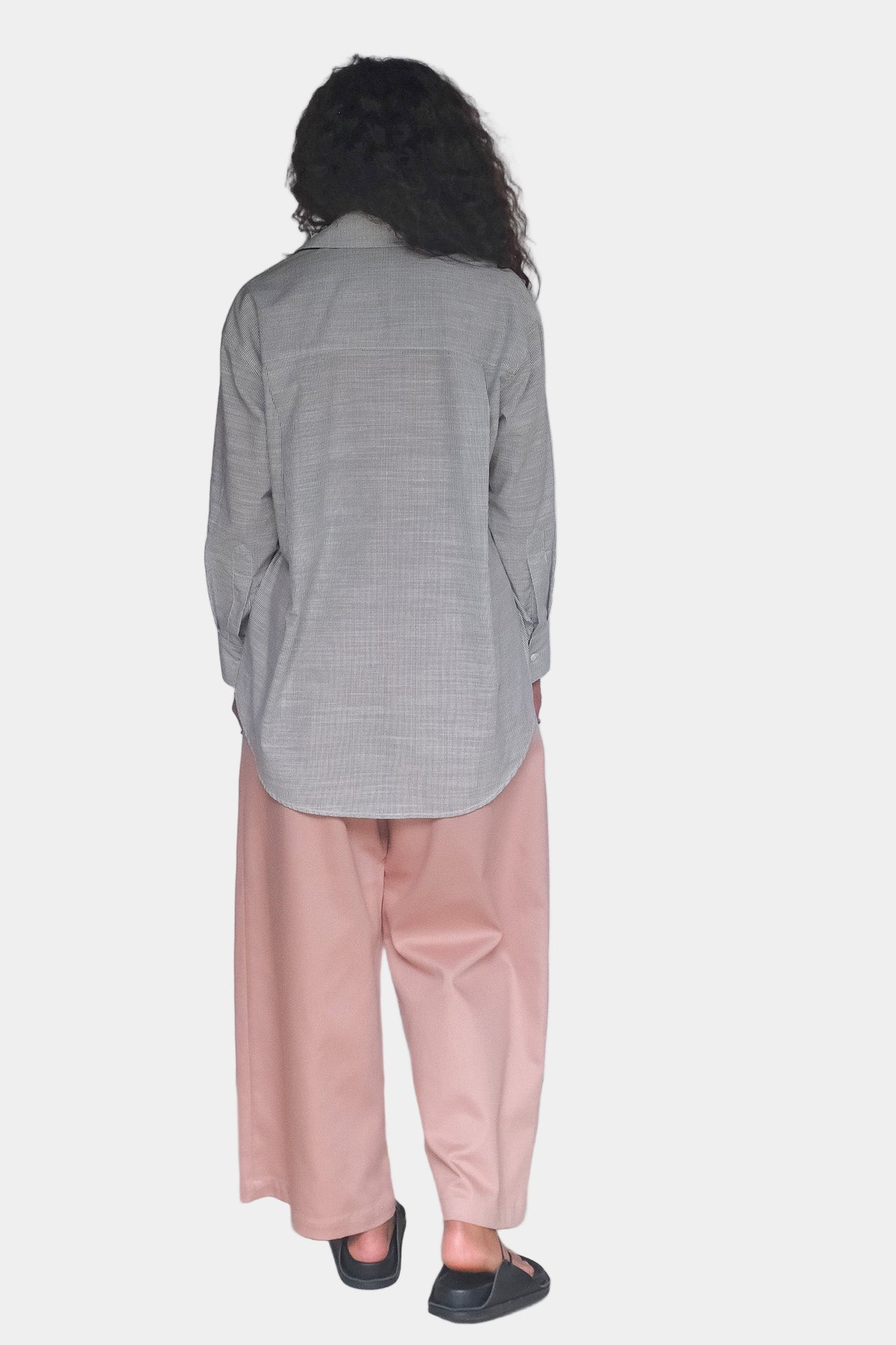 Person wearing a light gray shirt and pink pants against a white background