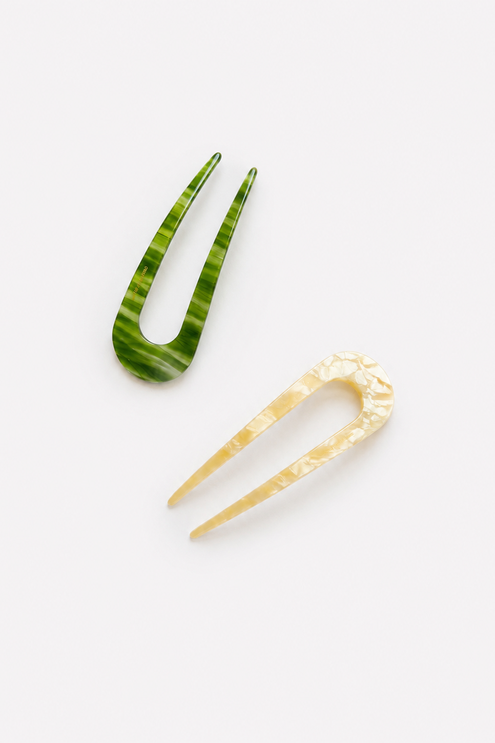 Two French hair pins on a plain white background, one with a green and white marbled pattern and the other in a textured pale cream finish - East Coast General