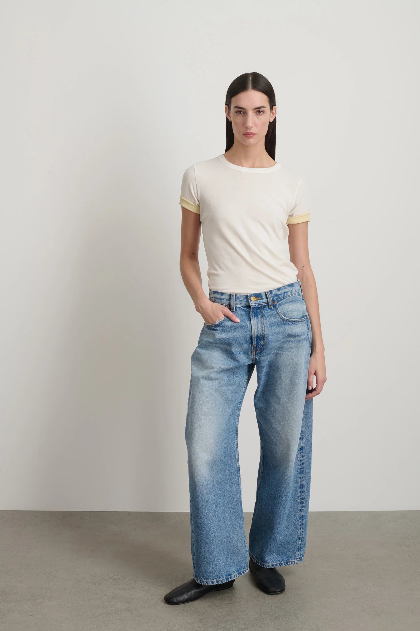 Woman wearing a white t-shirt and blue jeans against a plain background