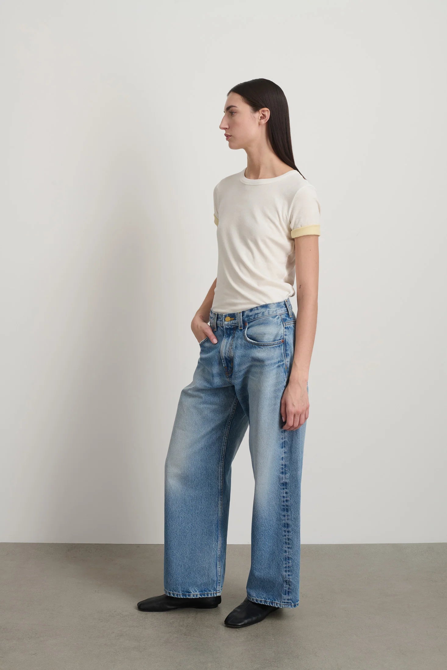 Woman wearing a white t-shirt and blue jeans standing against a plain background