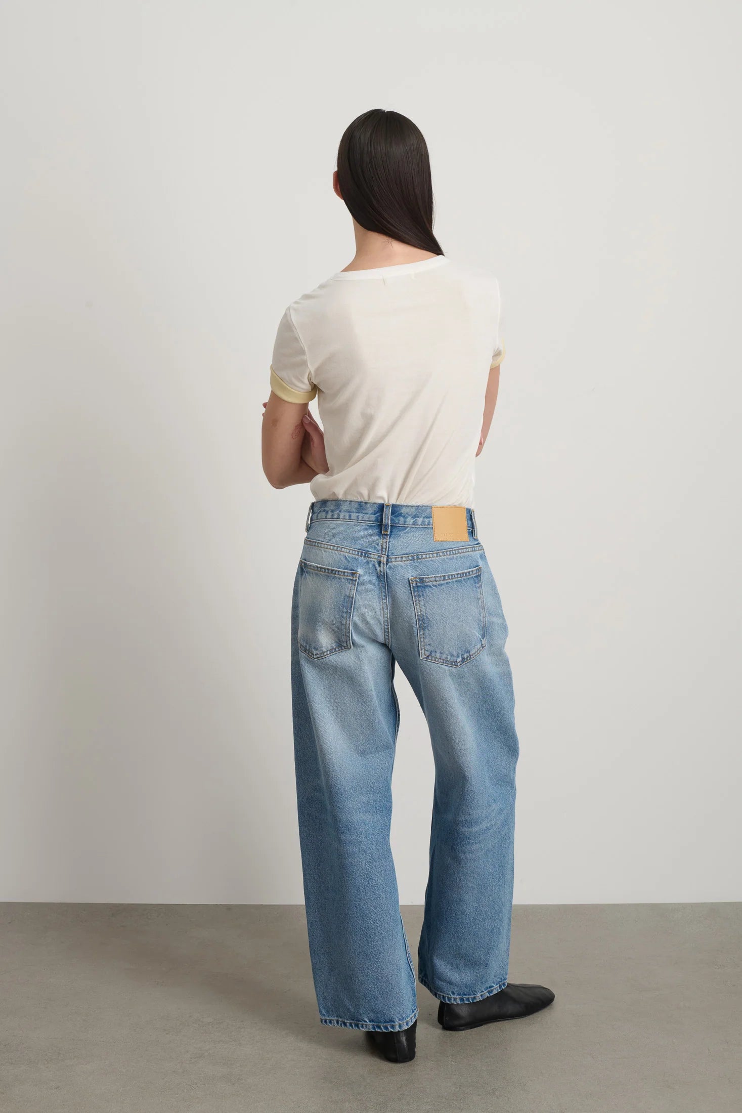 Person wearing light blue jeans and a white shirt from behind on a plain background