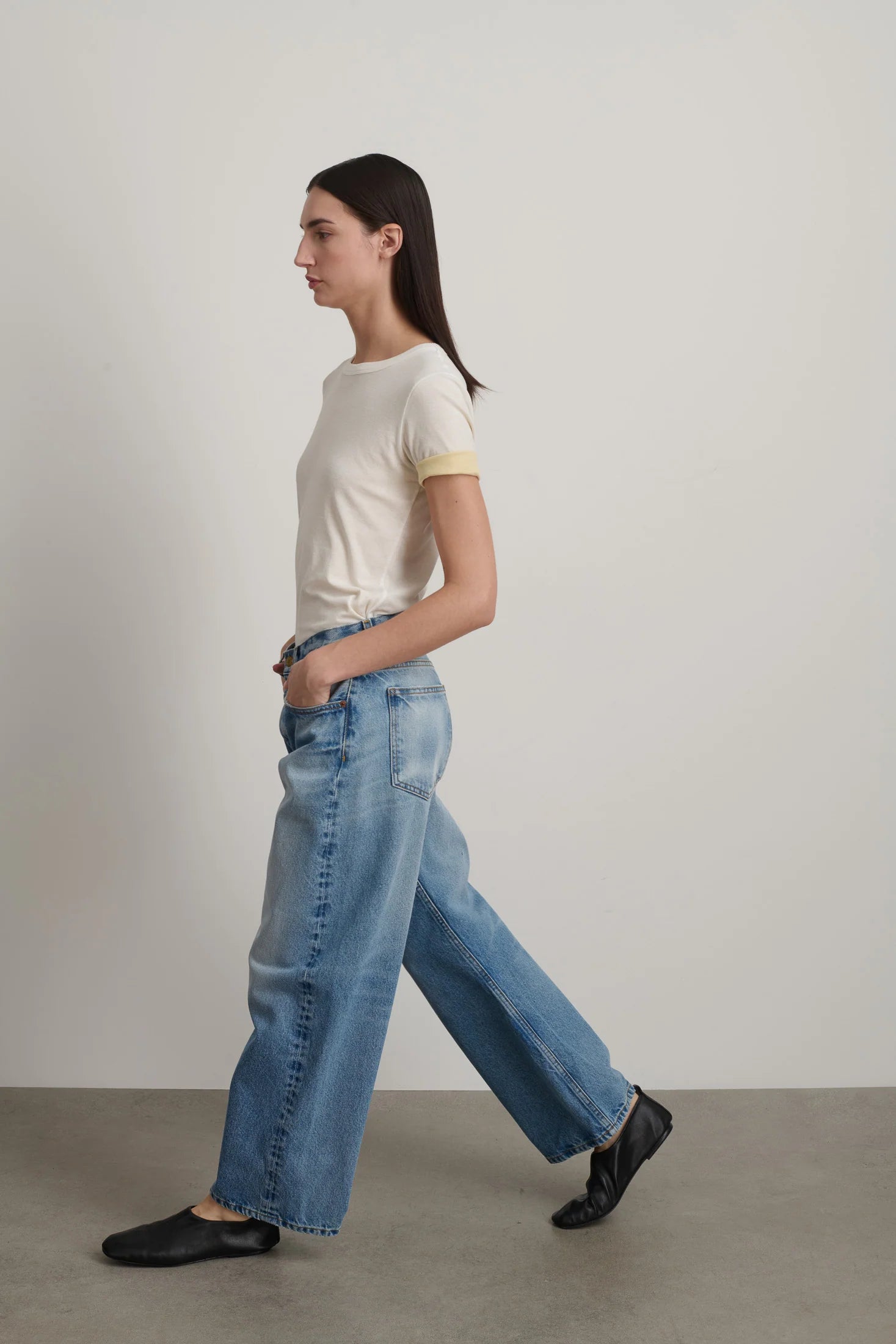 Woman wearing a white t-shirt and blue jeans walking on a plain background