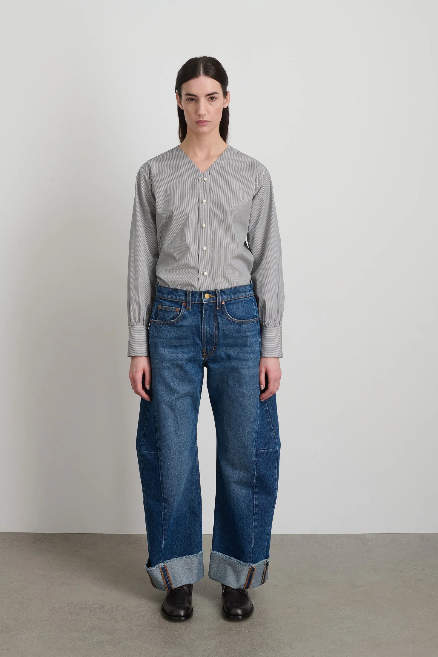 Person wearing a gray button-up shirt and blue jeans against a plain background