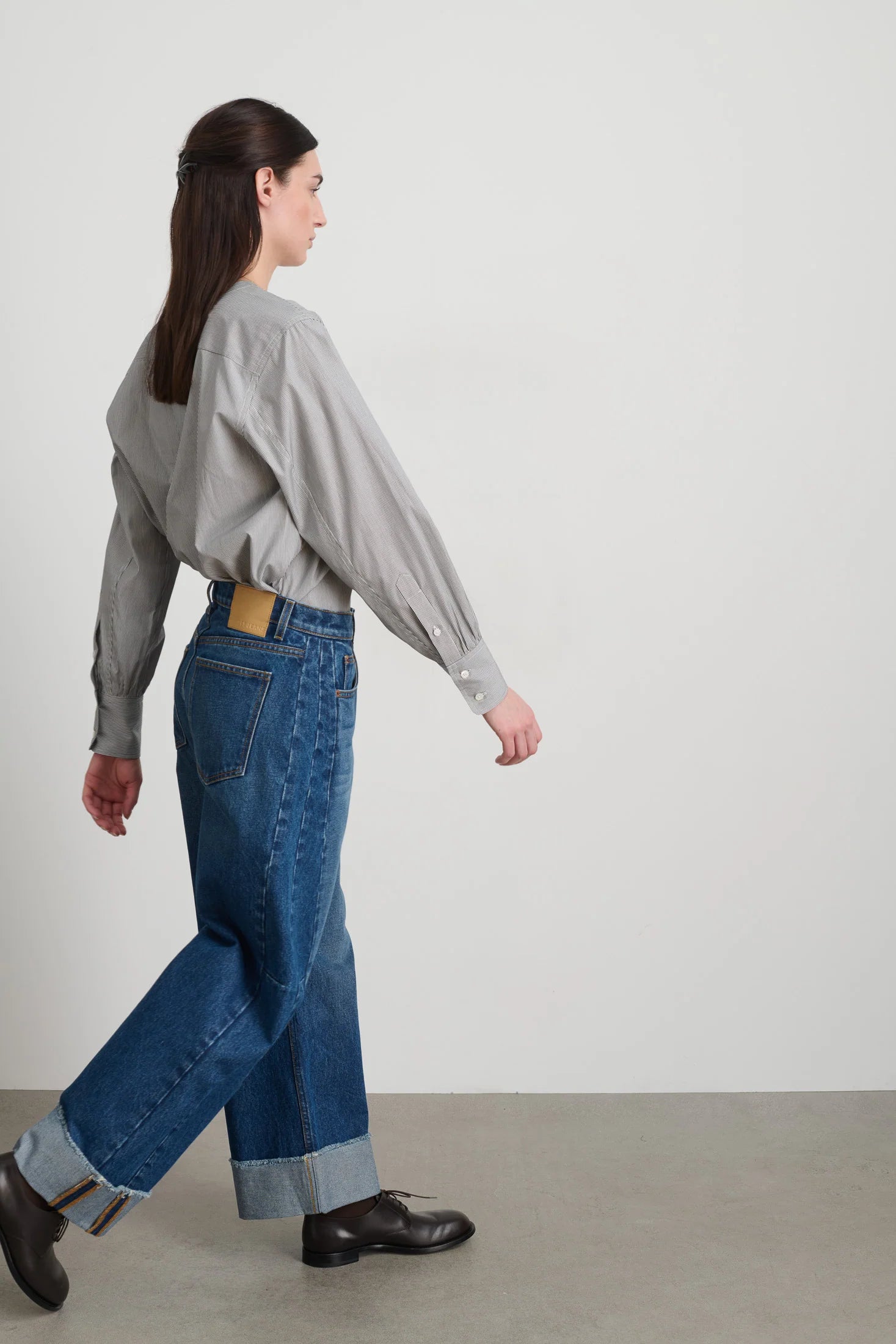 Person wearing a light gray sweater and blue jeans standing against a plain white background