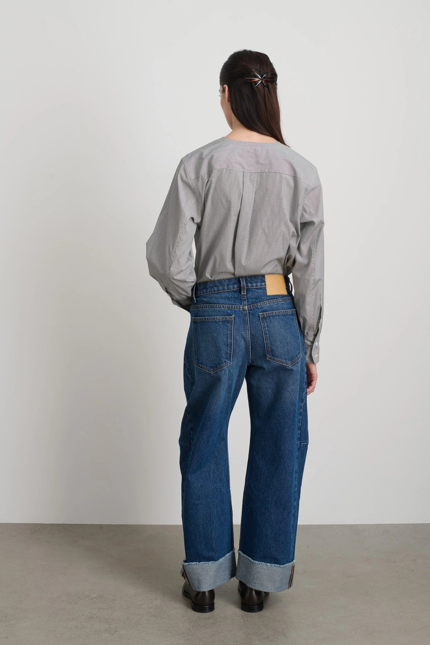 Person wearing a gray shirt and blue jeans standing against a plain white background