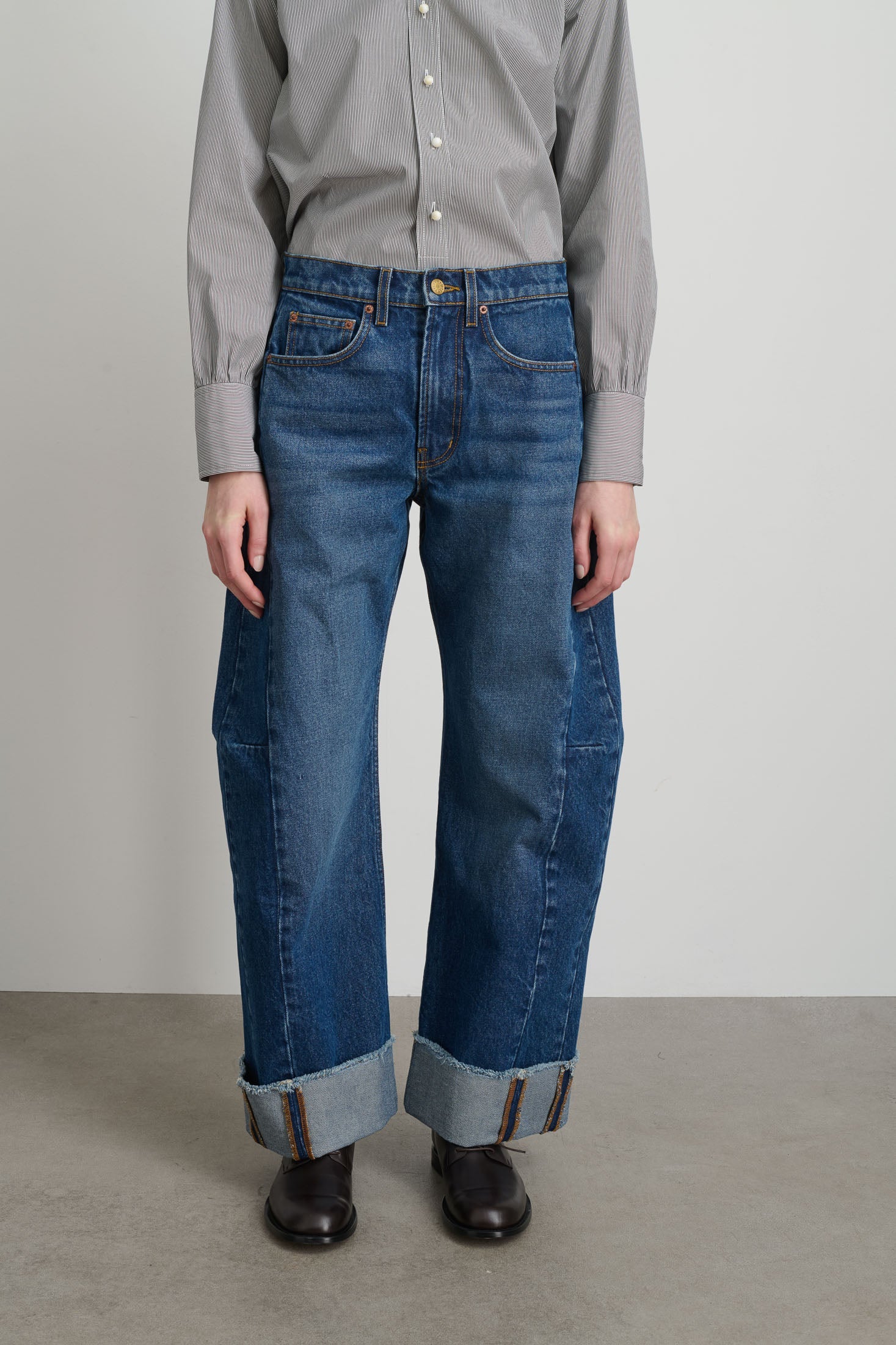 Person wearing blue jeans and a striped shirt against a plain background