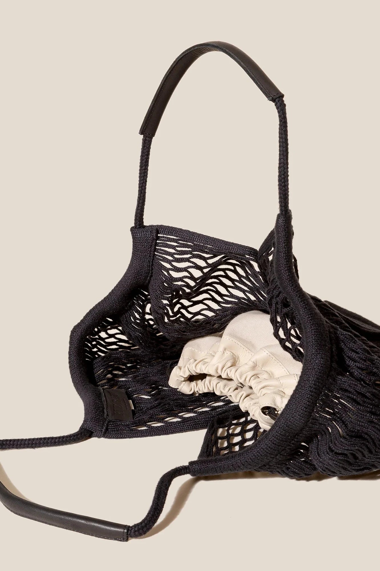 Black mesh bag with a beige interior holding white fabric on a beige background