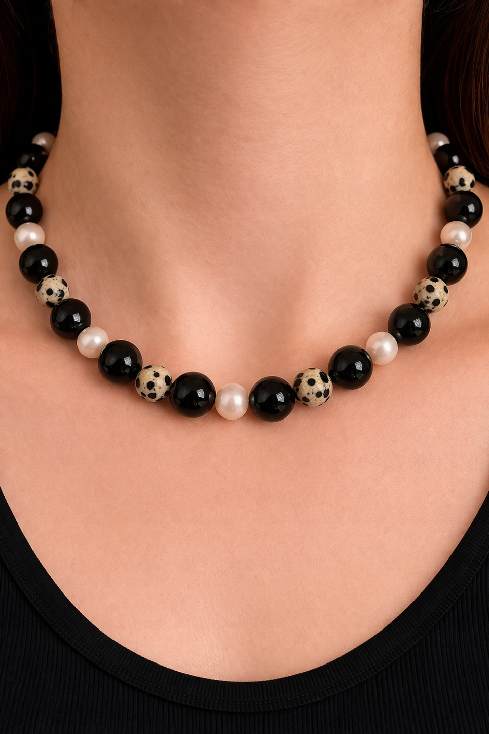 Necklace with freshwater pearls,  black onyx, and Dalmatian jasper beads on a person wearing a black top.