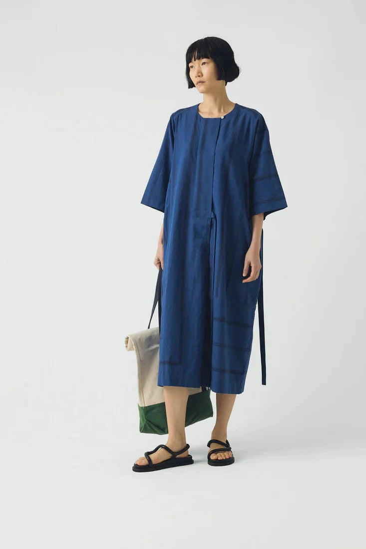 Woman wearing a blue dress holding a green and beige bag on a white background