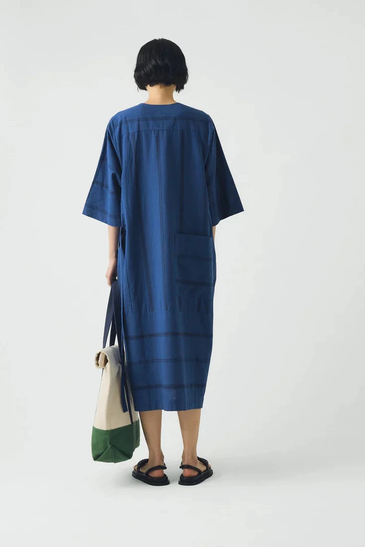 Person wearing a blue dress holding a green and beige bag on a white background