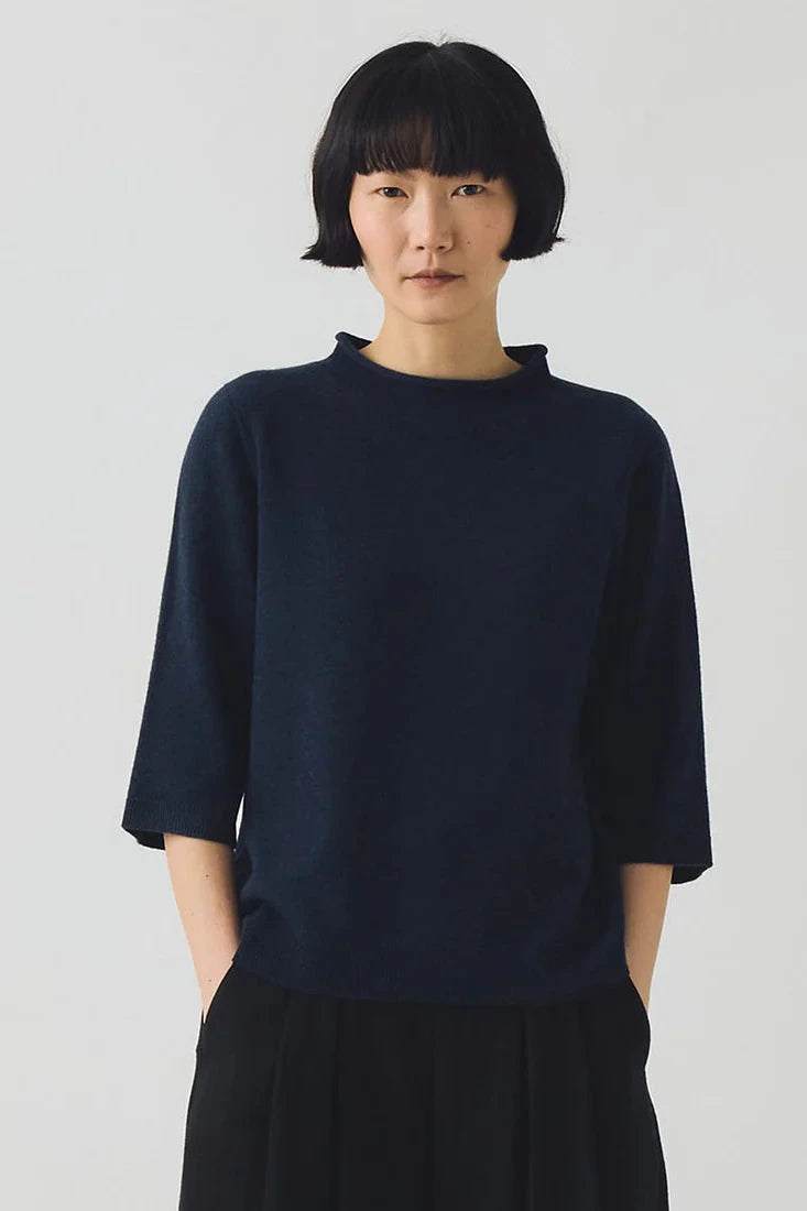 Person wearing a dark blue shirt against a plain background