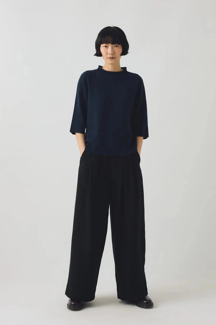 Person wearing a navy blue sweater and black wide-leg pants on a white background