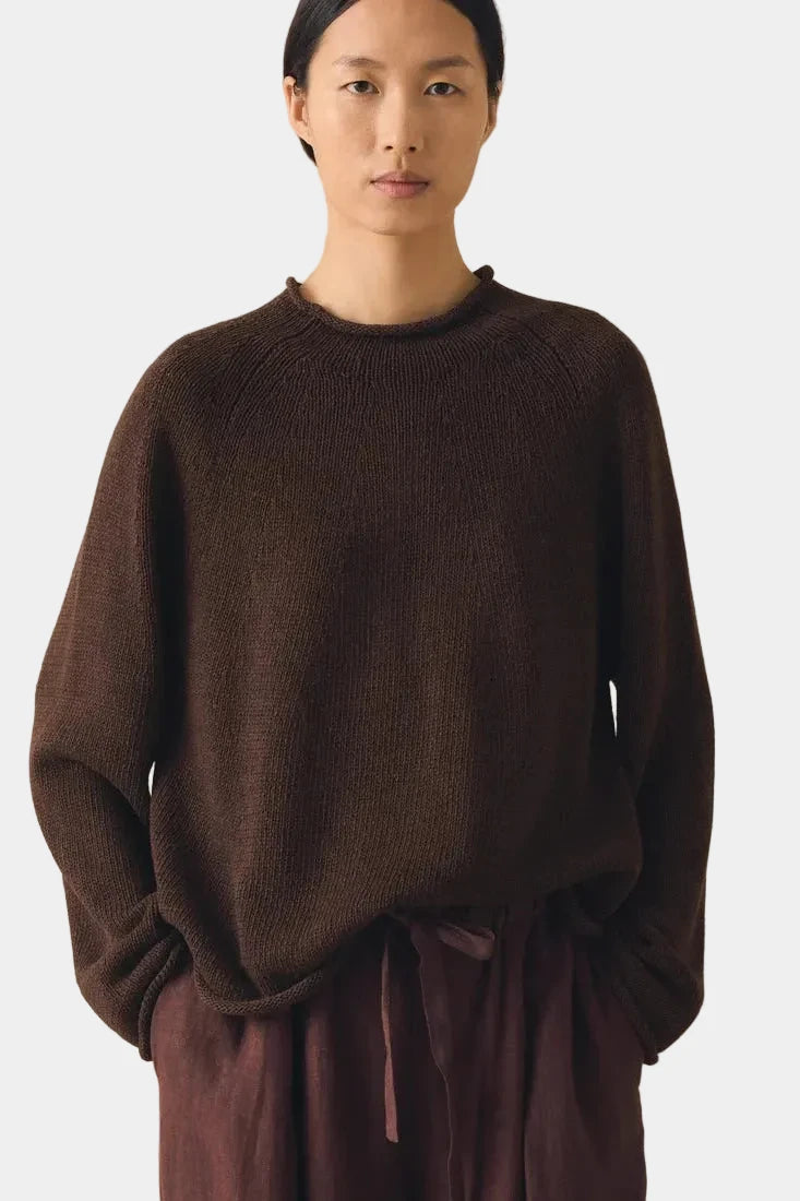 Person wearing a brown sweater and pants against a plain background