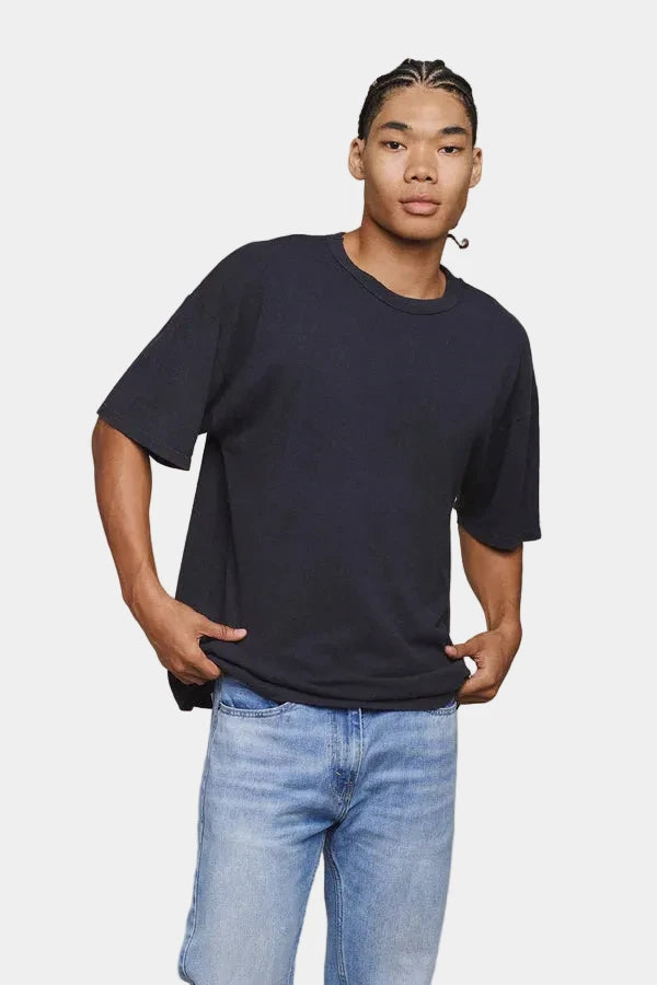 Person wearing a black t-shirt and blue jeans against a beige background