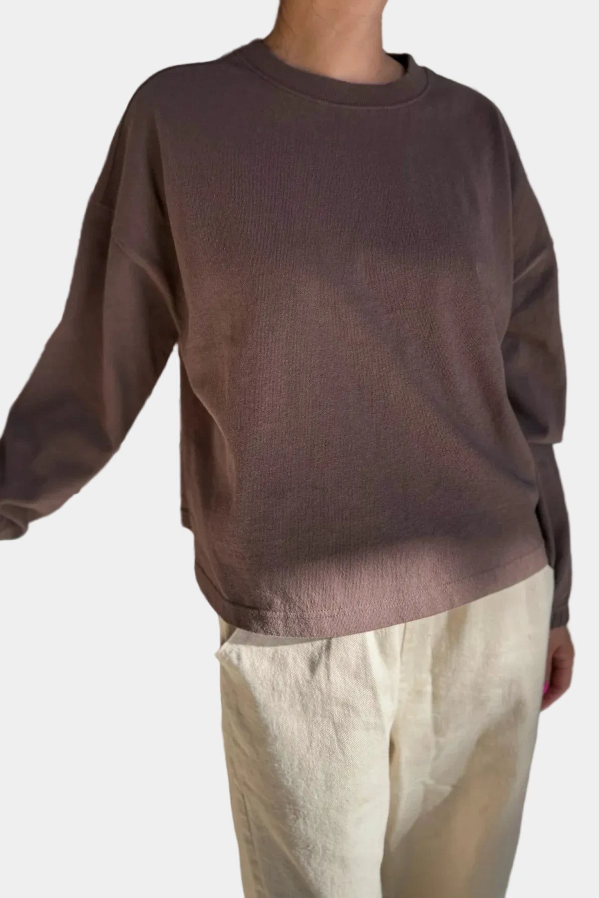 Person wearing a brown sweater and beige pants against a plain background
