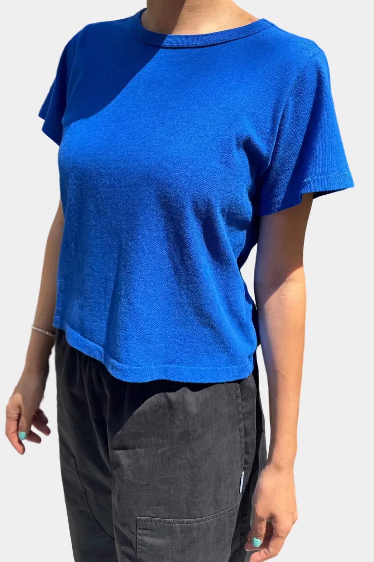Person wearing a blue shirt and black pants standing against a plain background