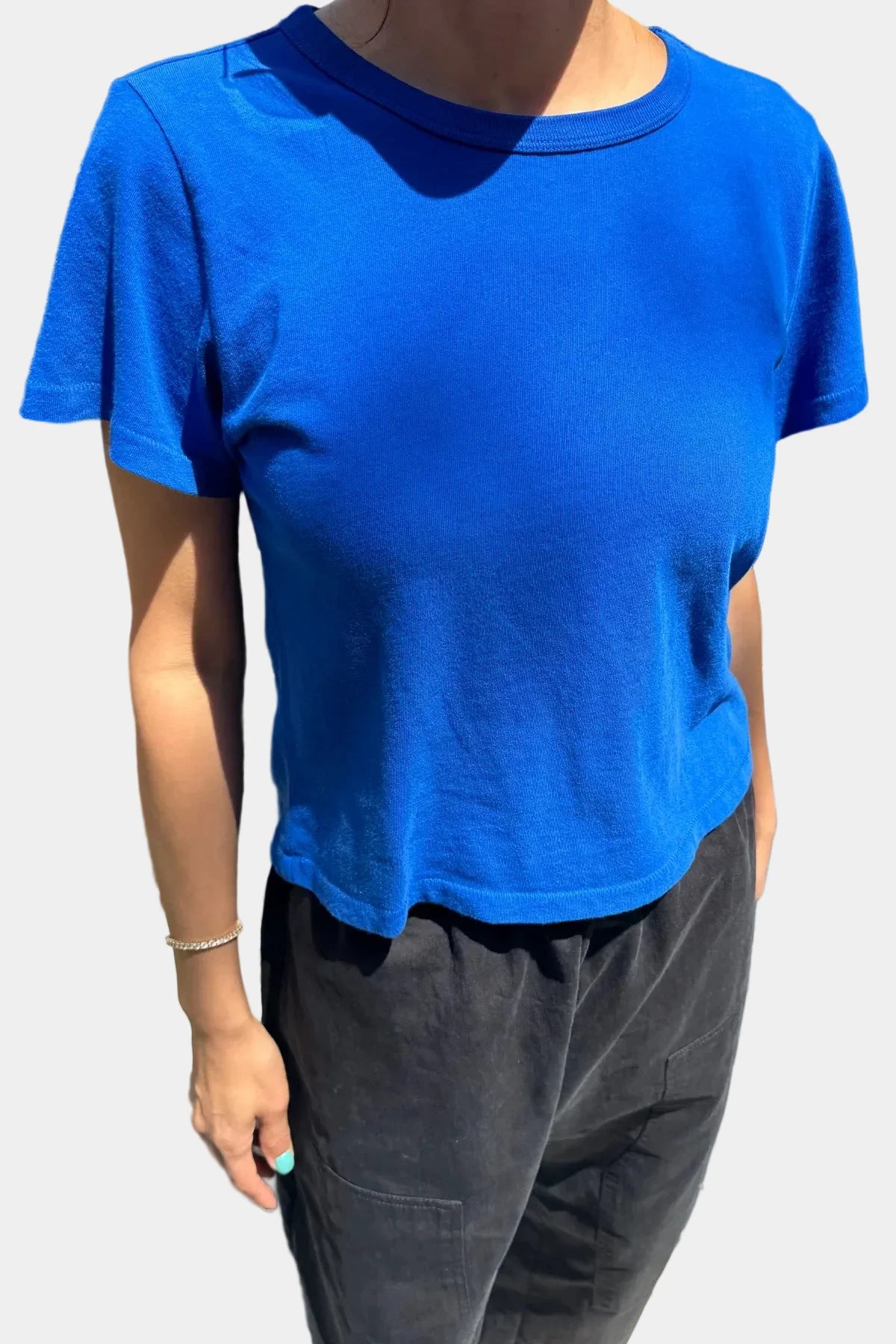 Person wearing a blue t-shirt and dark pants standing against plain background