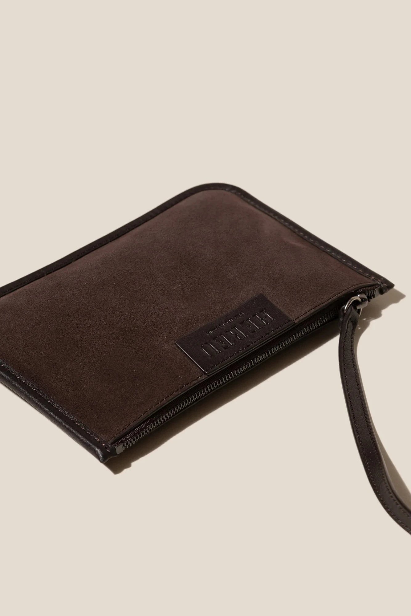 Brown leather wristlet with a visible brand logo on a beige background