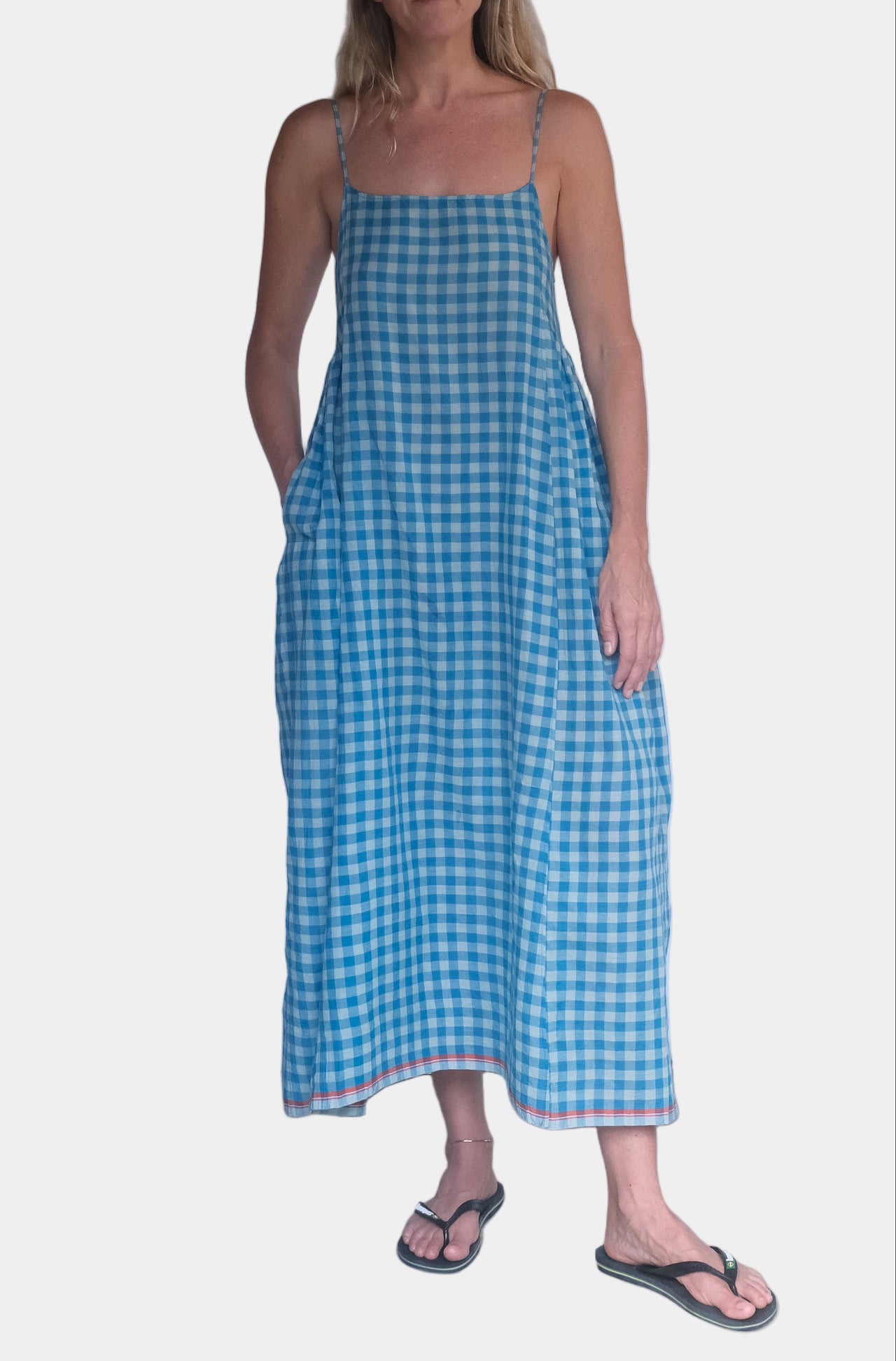 Woman wearing a blue checkered dress standing against a white wall.