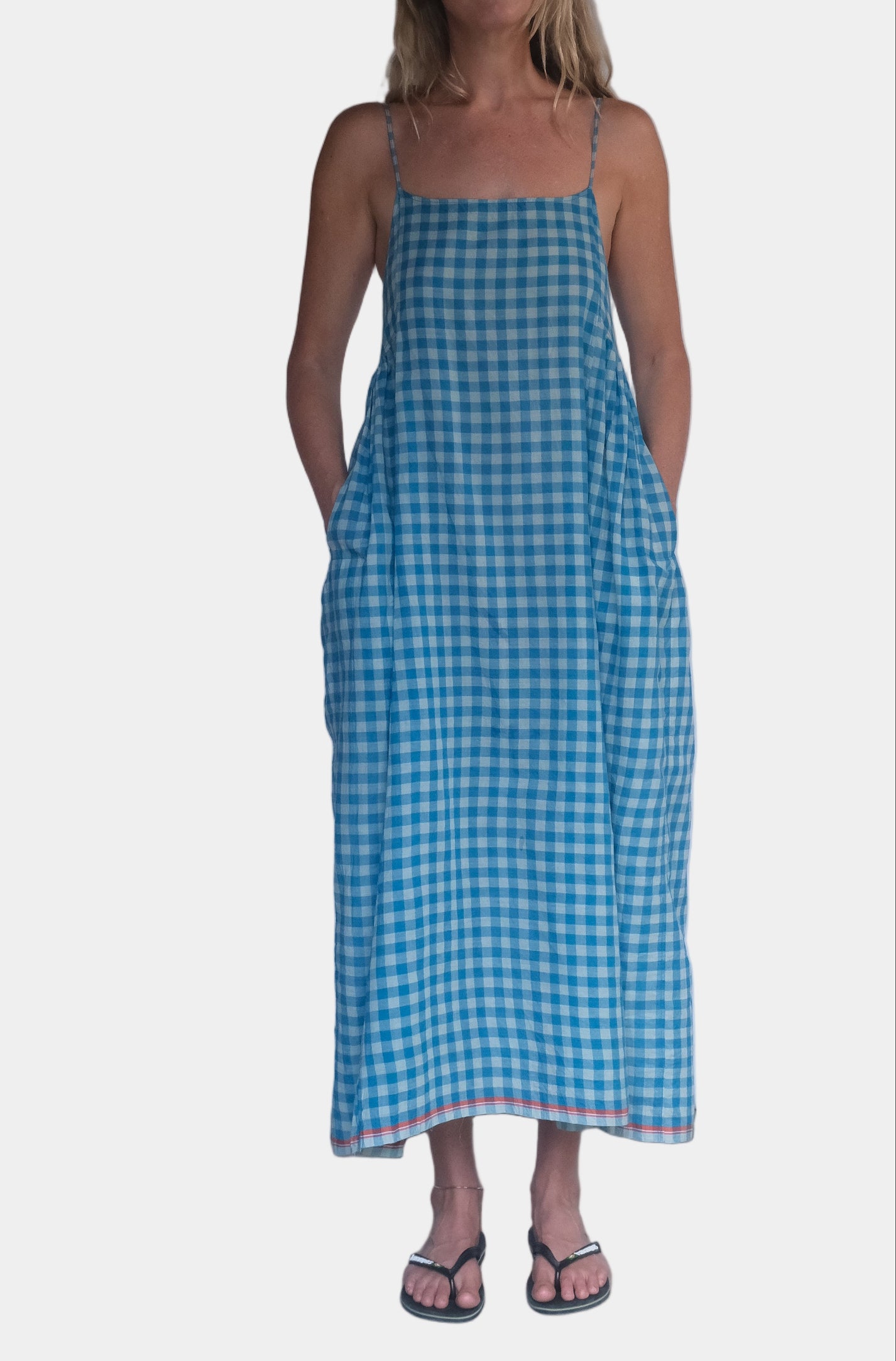 Woman wearing a blue checkered dress standing against a white wall.