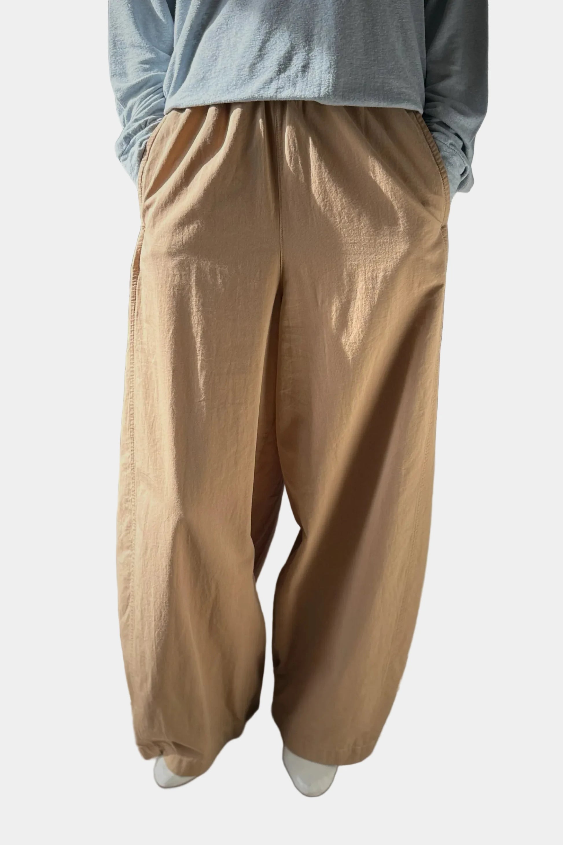 Person wearing beige wide-leg pants and a light blue shirt against a plain background